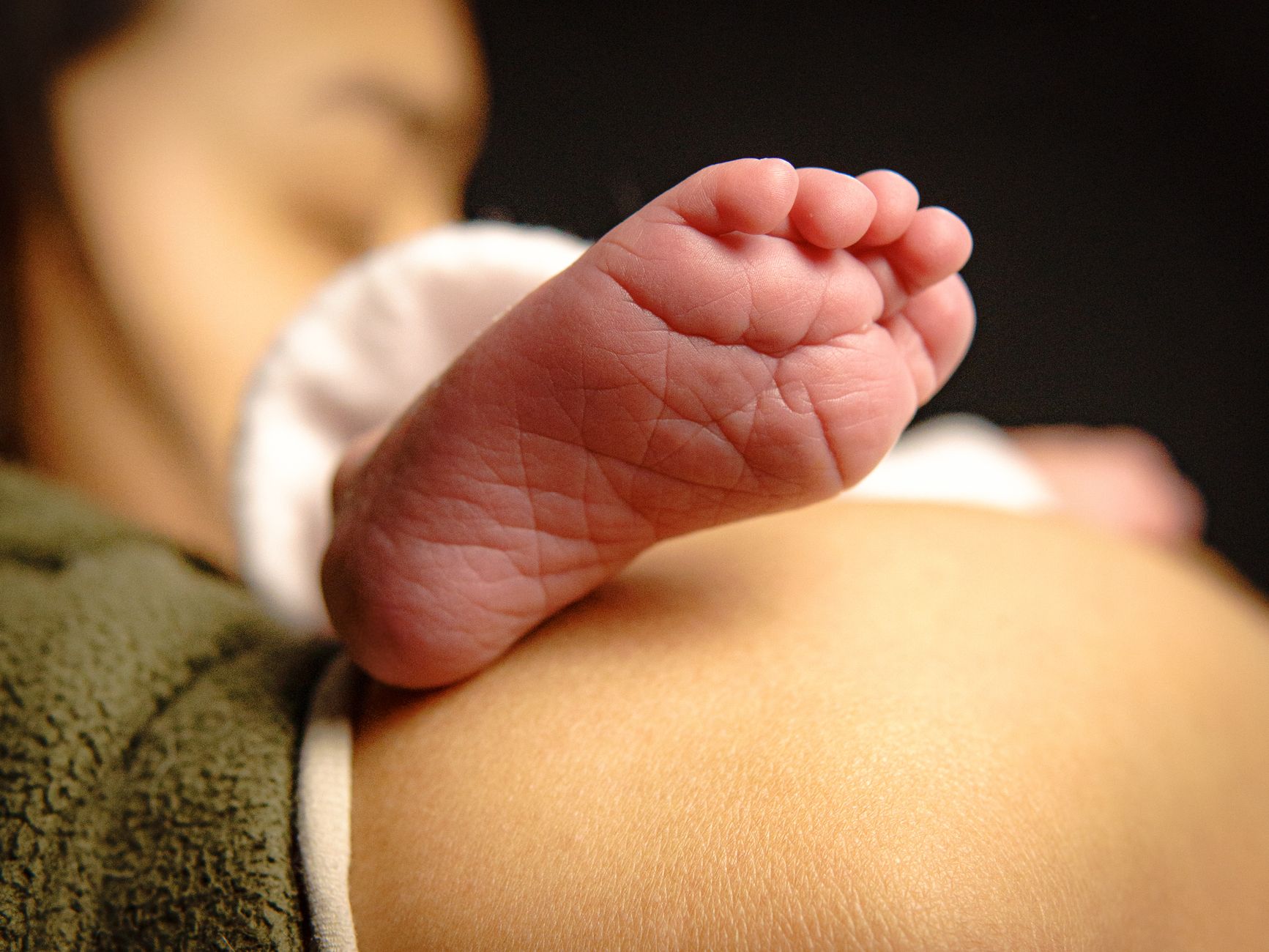 Parent gently patting a baby's back while holding them upright against the chest, soft natural light, warm home setting