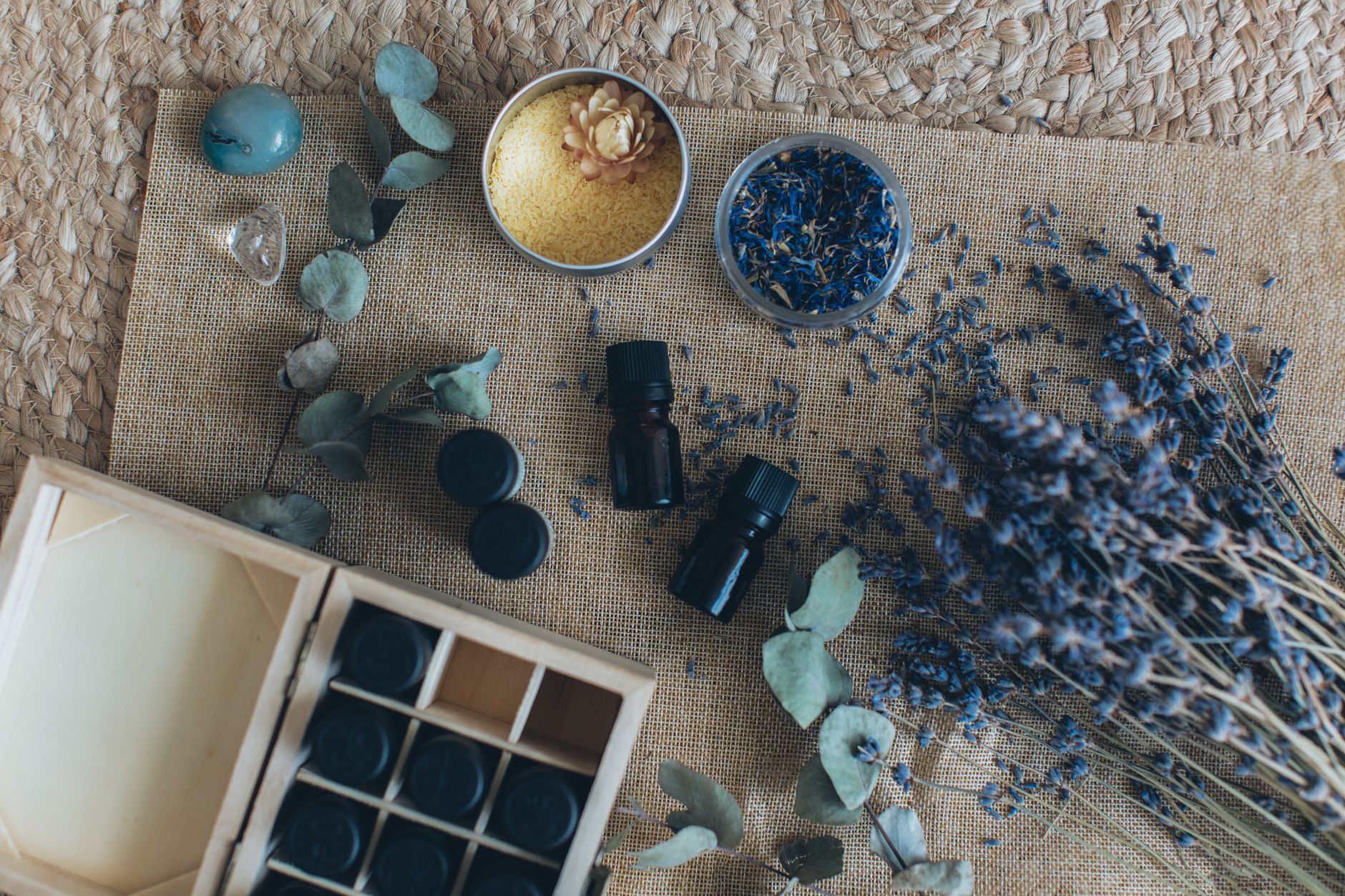 A wooden board displaying a variety of stretch‑mark creams, natural oils, and a fresh sprig of lavender, bright natural light highlighting product textures