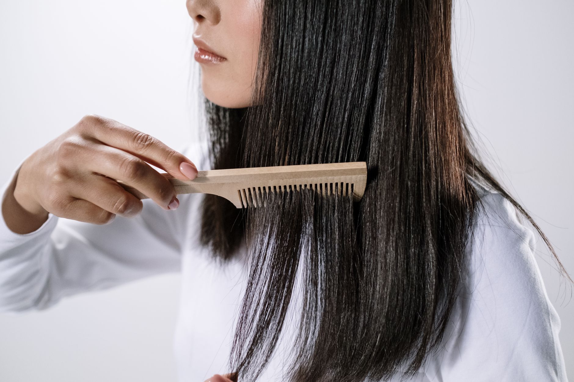 A woman gently brushing her long hair with a wide-tooth comb, focusing on the ends, with a soft, natural background
