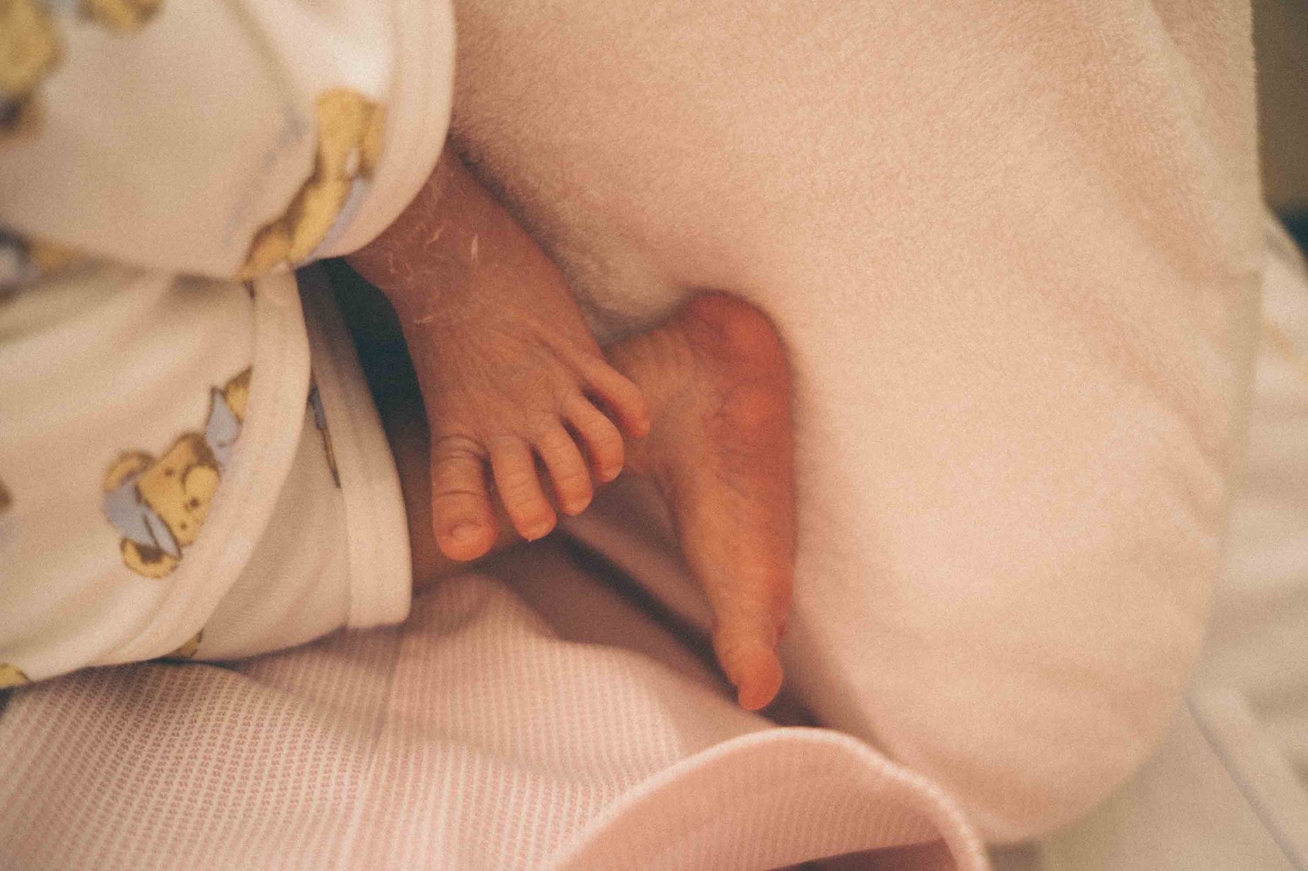 A soft‑focused photograph of a newborn’s foot being gently held while a transcutaneous bilirubinometer is placed on the skin, natural daylight through a window