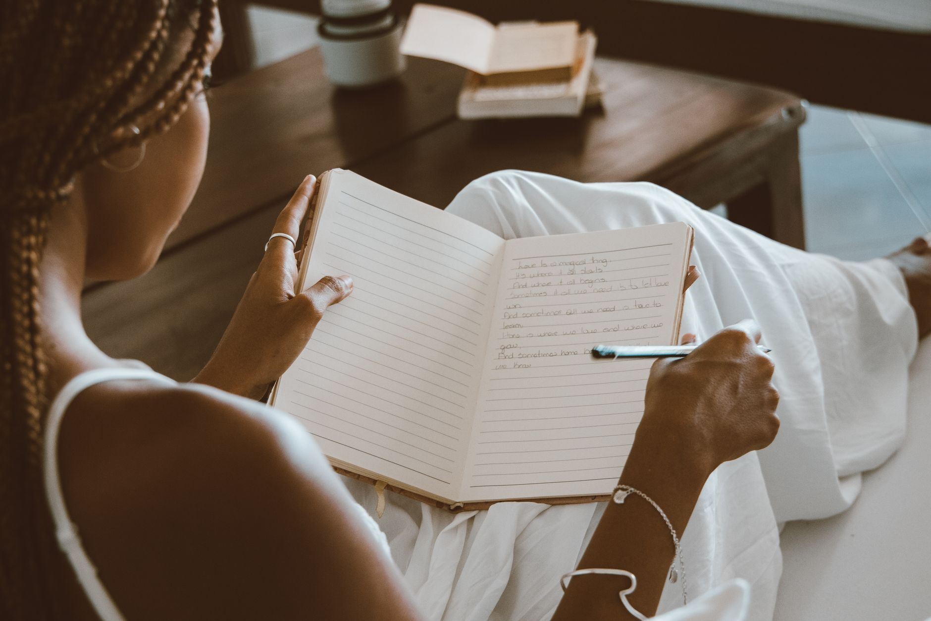 A Black mother sitting on a bed with her hands on her face, looking exhausted but supported by a stack of books and a journal