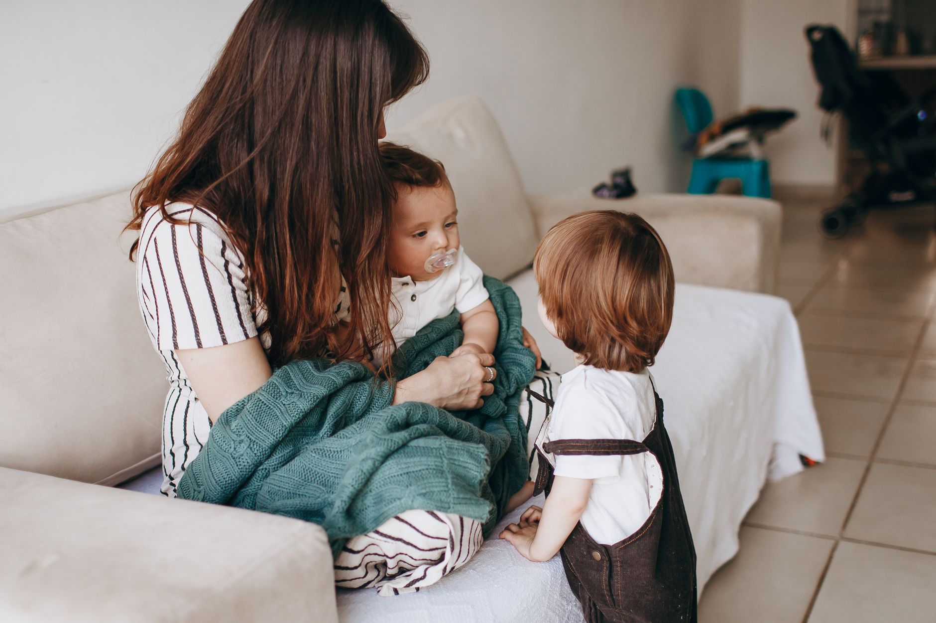 A mother sitting on a couch with her two children, one toddler and one baby, both looking content