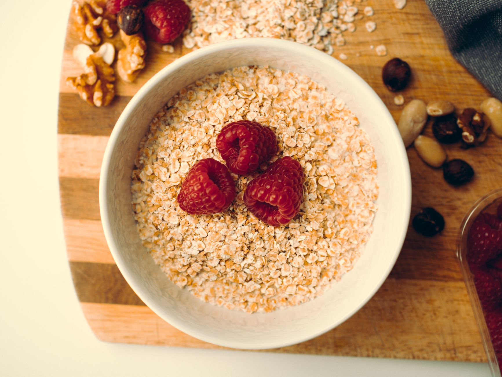 A glass of water, a handful of almonds, and a bowl of oatmeal on a wooden countertop, representing hydration and nutrition for lactating parents