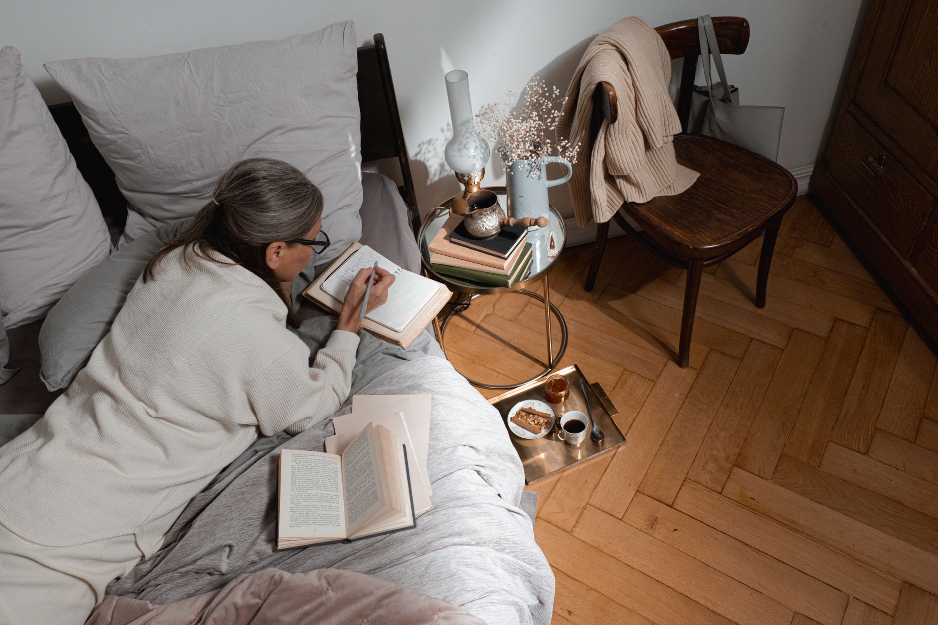 A cozy bedside table with a glass of water, a soft blanket, and a notebook labeled ‘Postpartum Tracker’ beside a sleeping newborn