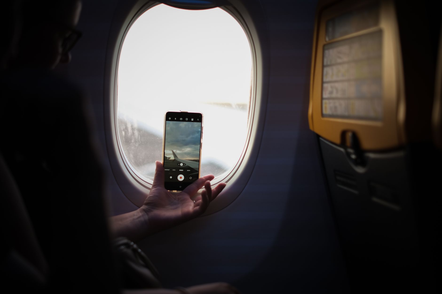 A woman checking her phone for fertility tracking while sitting on a plane, soft cabin light, photorealistic