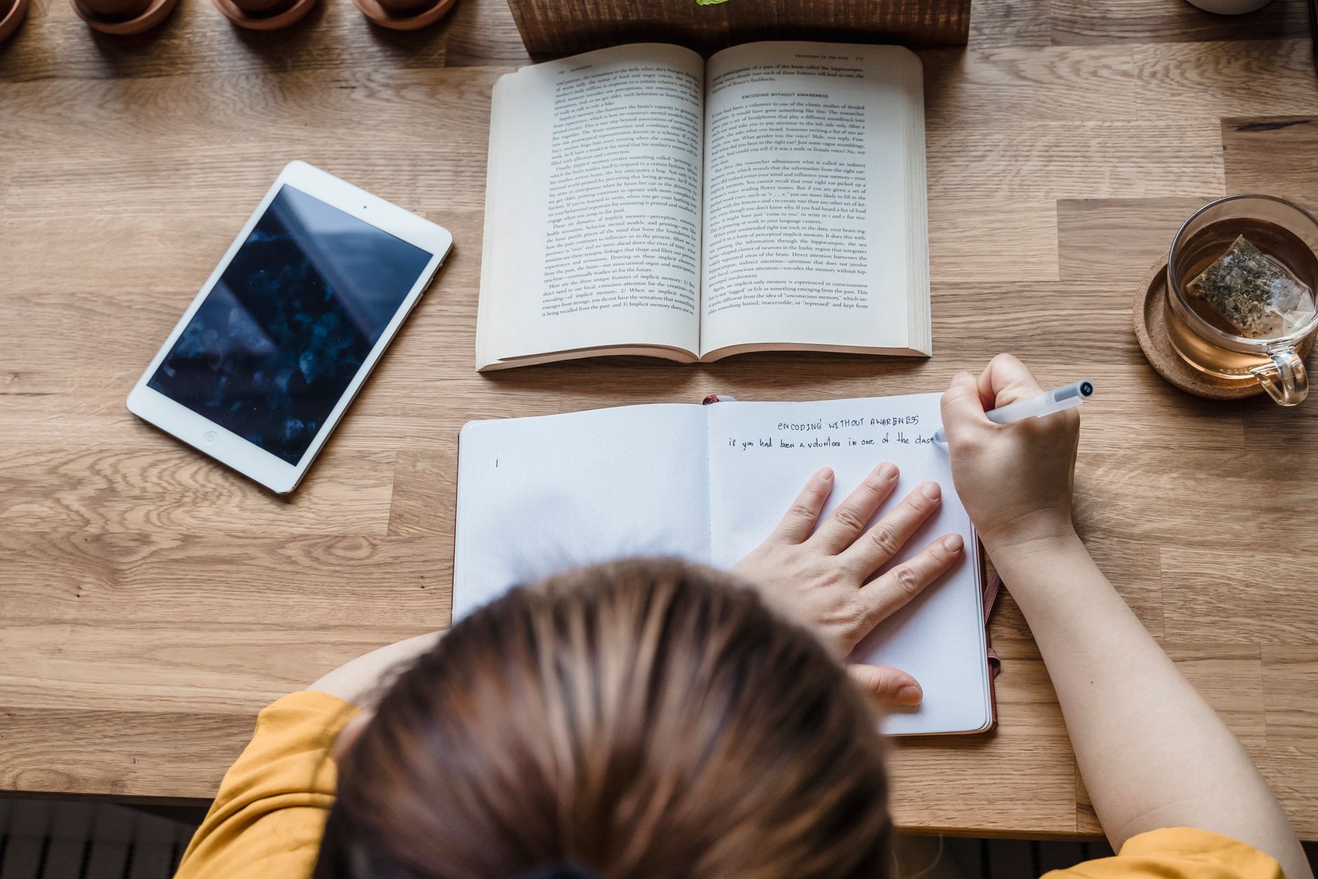 A woman sitting at a kitchen table with a cup of tea, a pregnancy test in hand, and a notebook open to a list of questions for her doctor, soft daylight streaming through a window