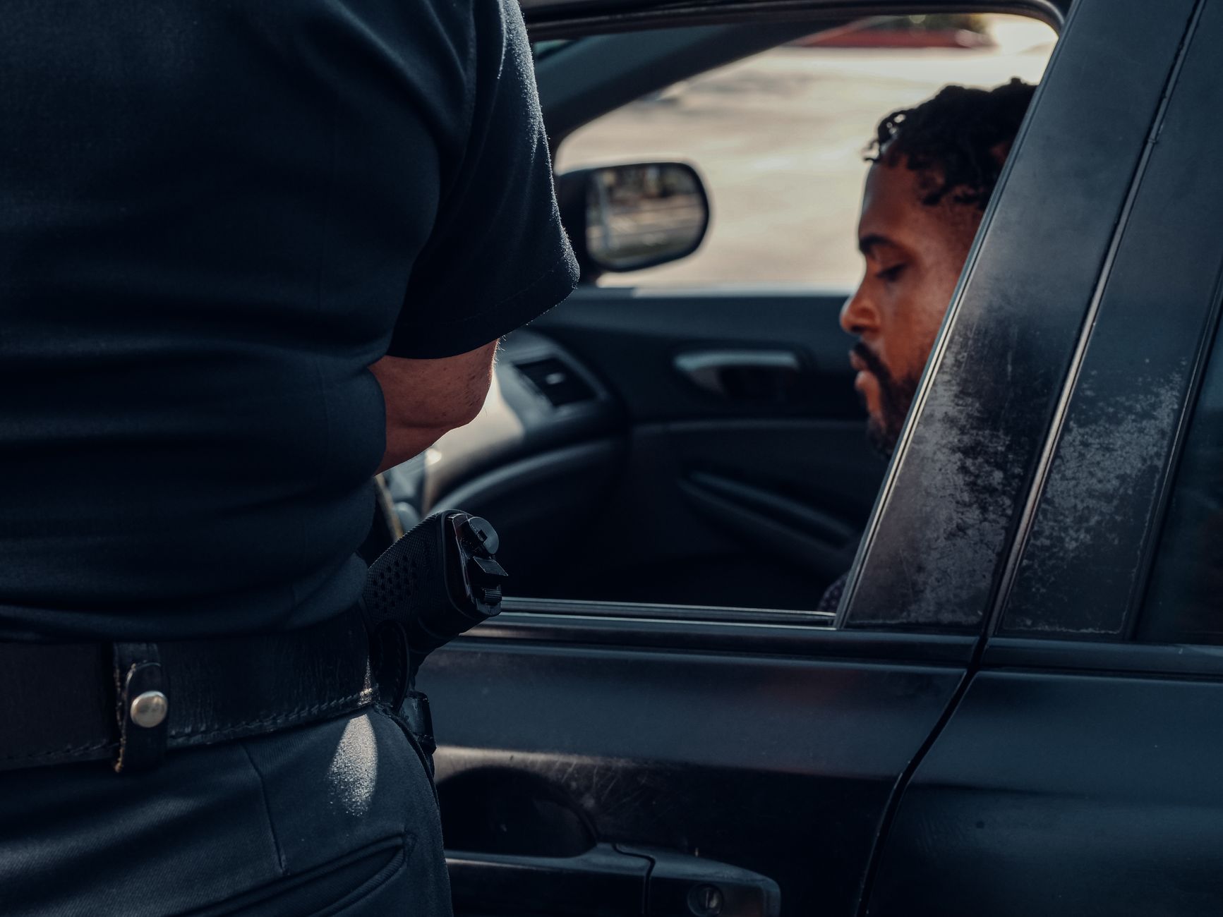 A police officer's hand holding a ticket book, with a blurred car interior and car seat in the background.