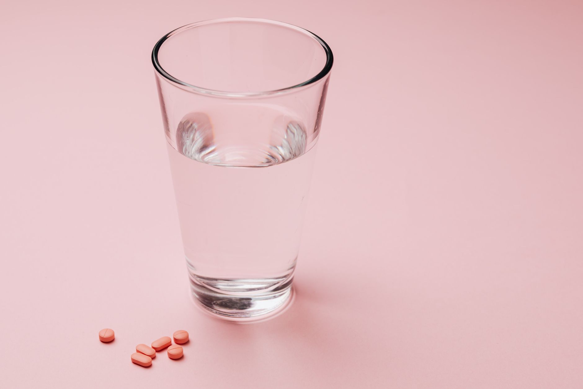 A hand holding a small tube of vaginal progesterone gel beside a glass of water on a pastel kitchen counter, natural morning light