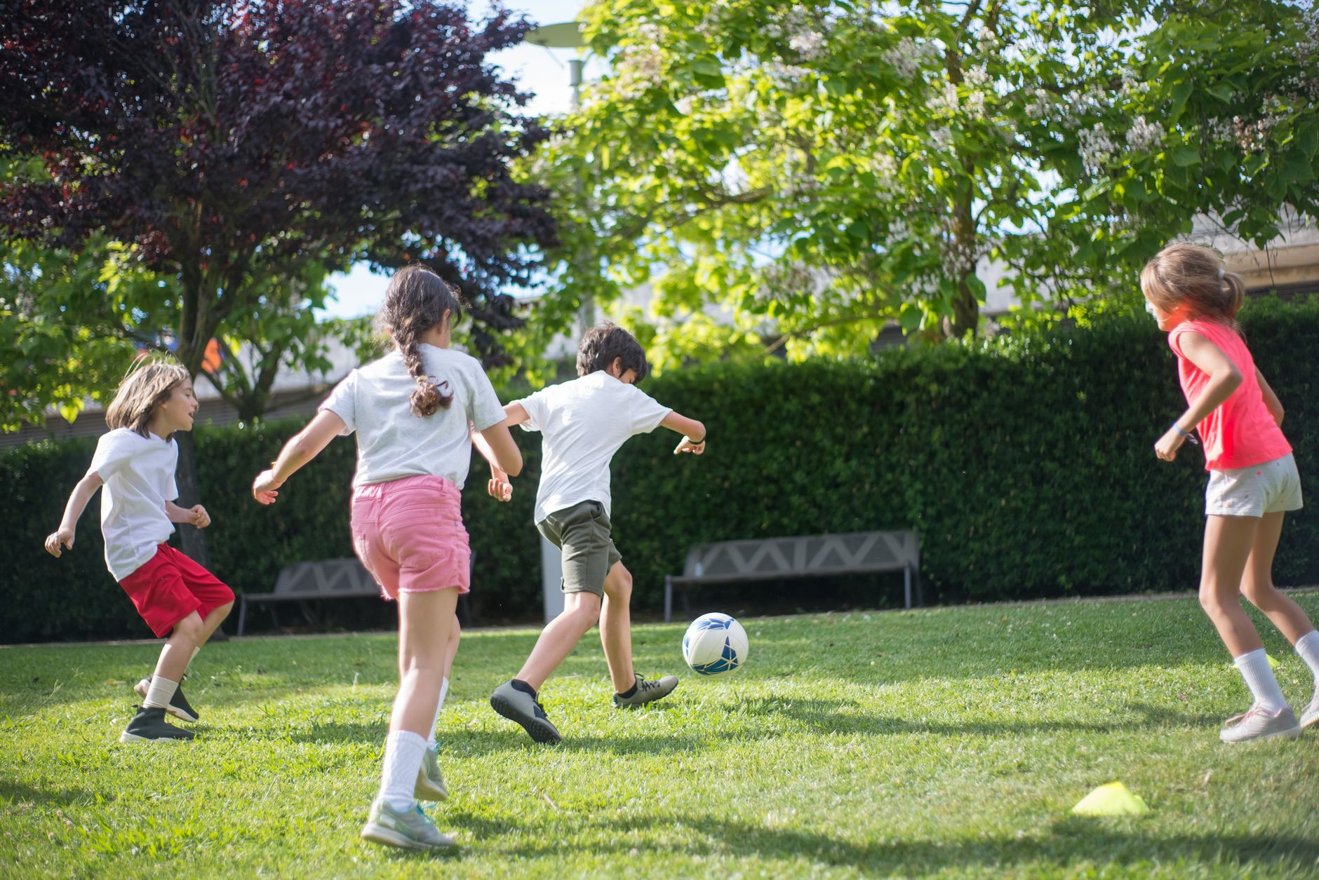 A diverse group of children laughing and playing soccer in a sunny park, demonstrating active play
