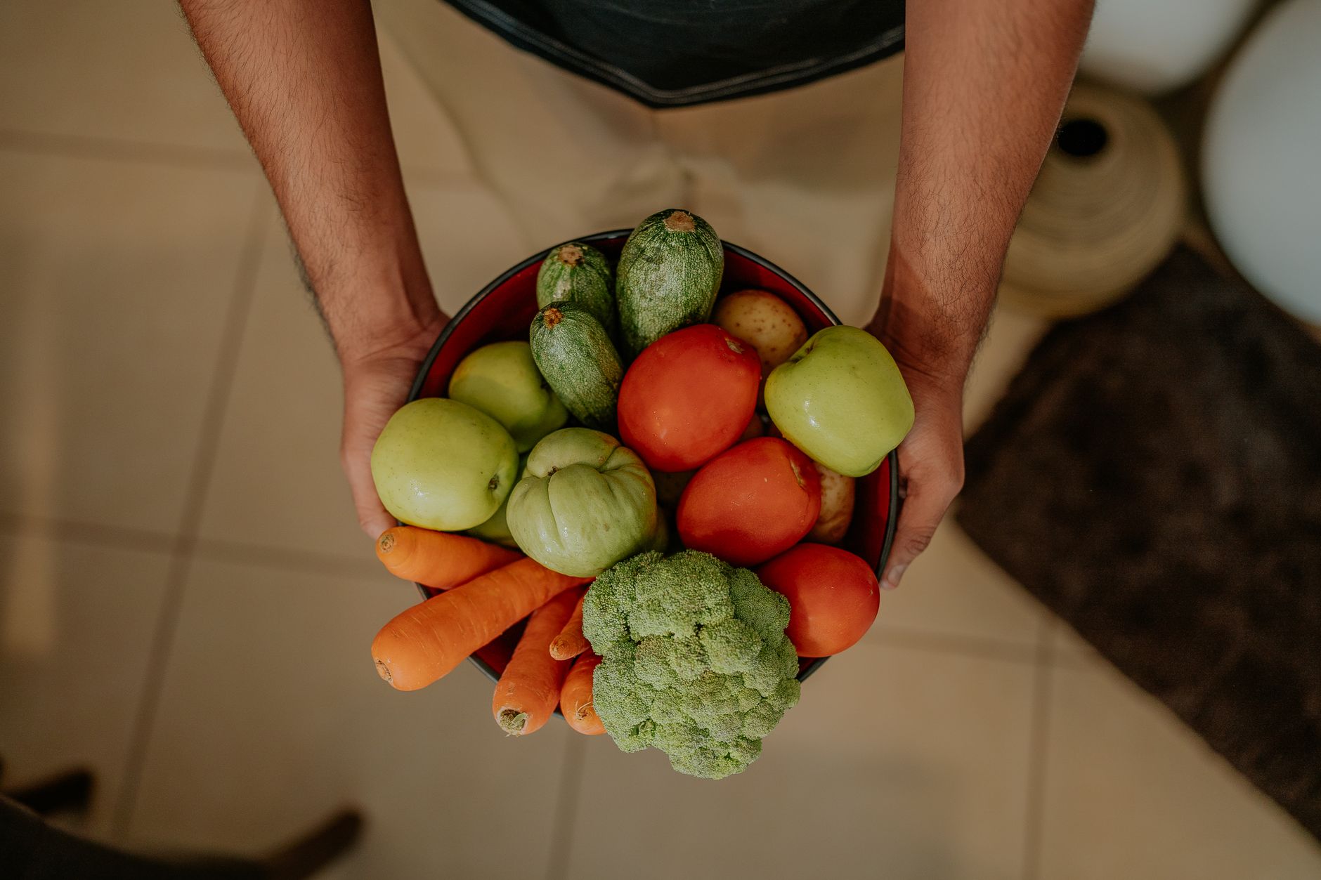 Diverse fresh fruits and vegetables artfully arranged on a wooden table, with child's hands reaching for an apple