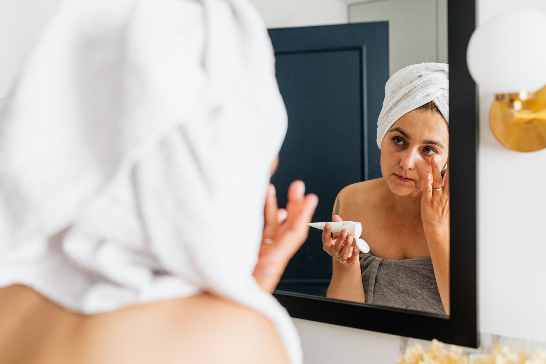 A breastfeeding mom applying clean beauty product with her baby nearby
