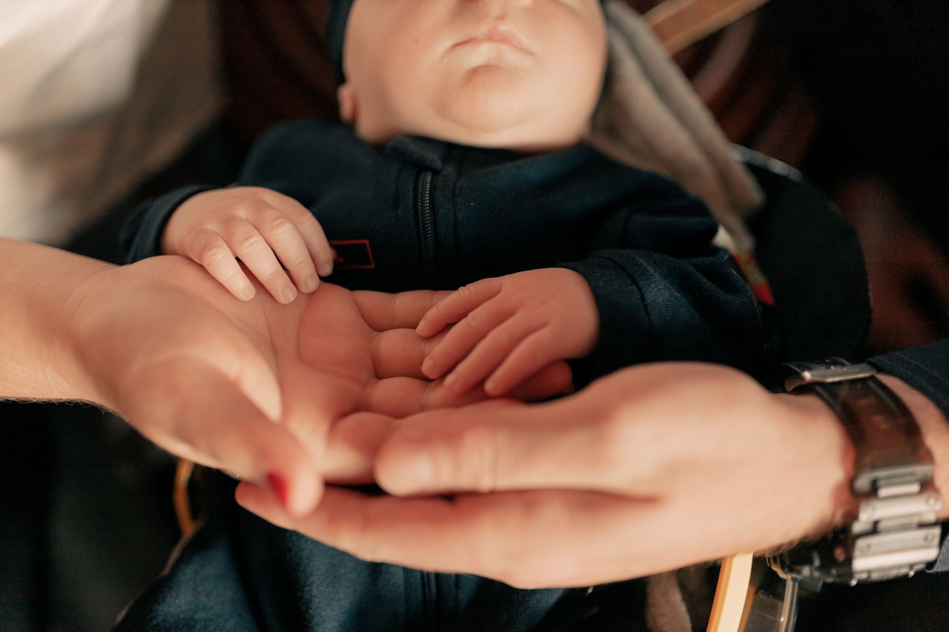 A tiny newborn baby in a NICU incubator, with parents' hands gently touching the incubator glass, their faces blurred in the background.