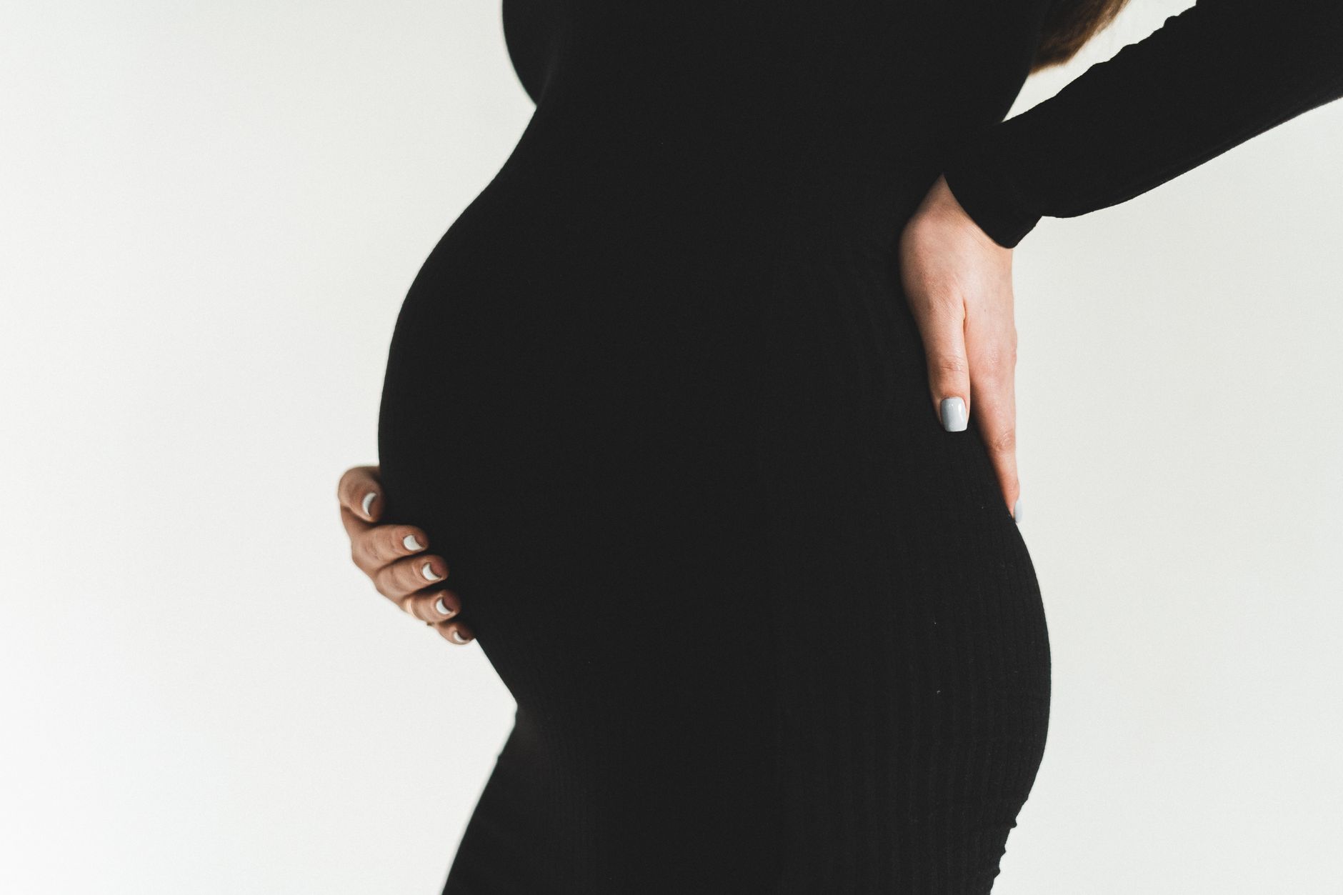 Pregnant woman performing a pelvic tilt against a wall, demonstrating proper posture