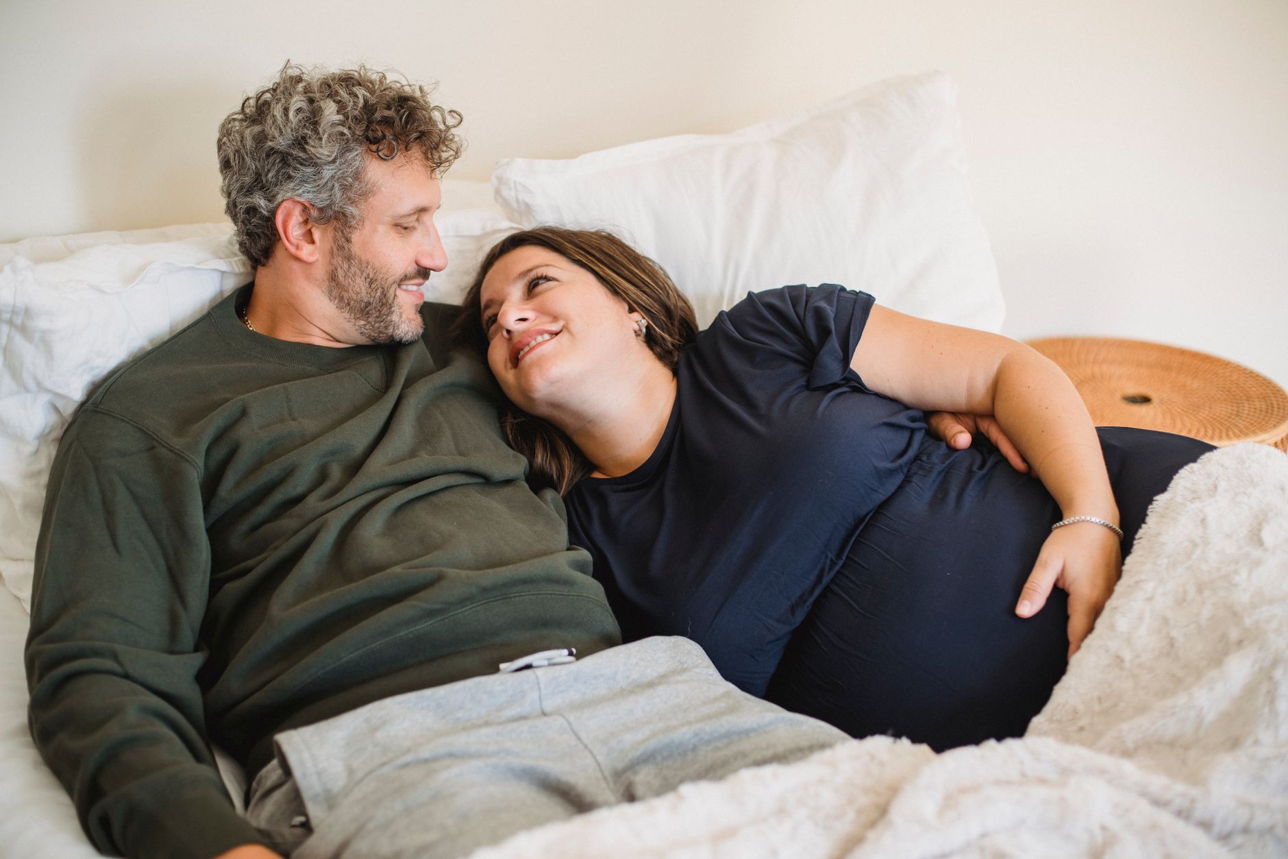 A couple sitting on a couch, laughing and holding hands while looking at a baby monitor