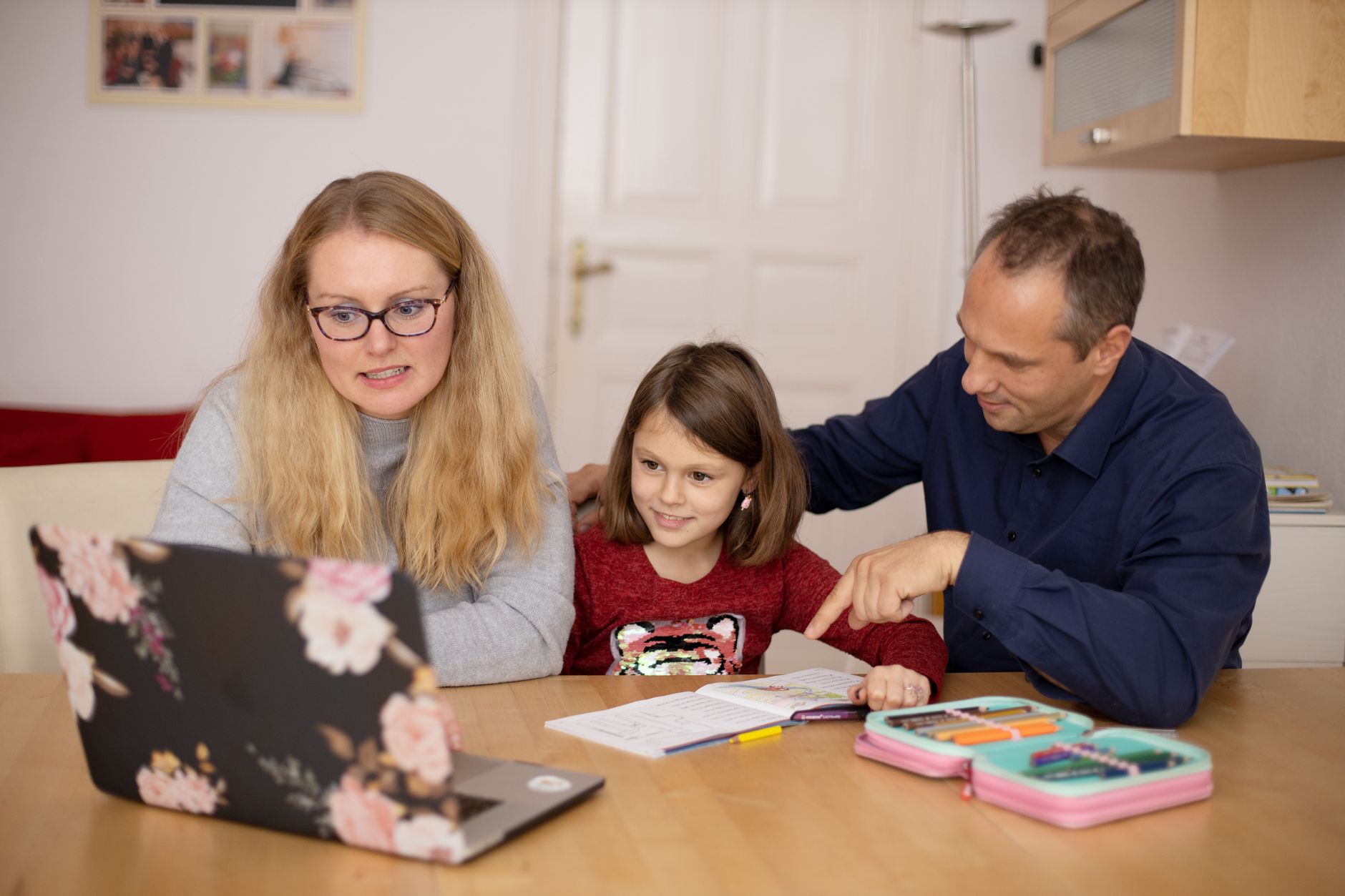 Two parents sitting at a table with their child, smiling, surrounded by school supplies and snacks.