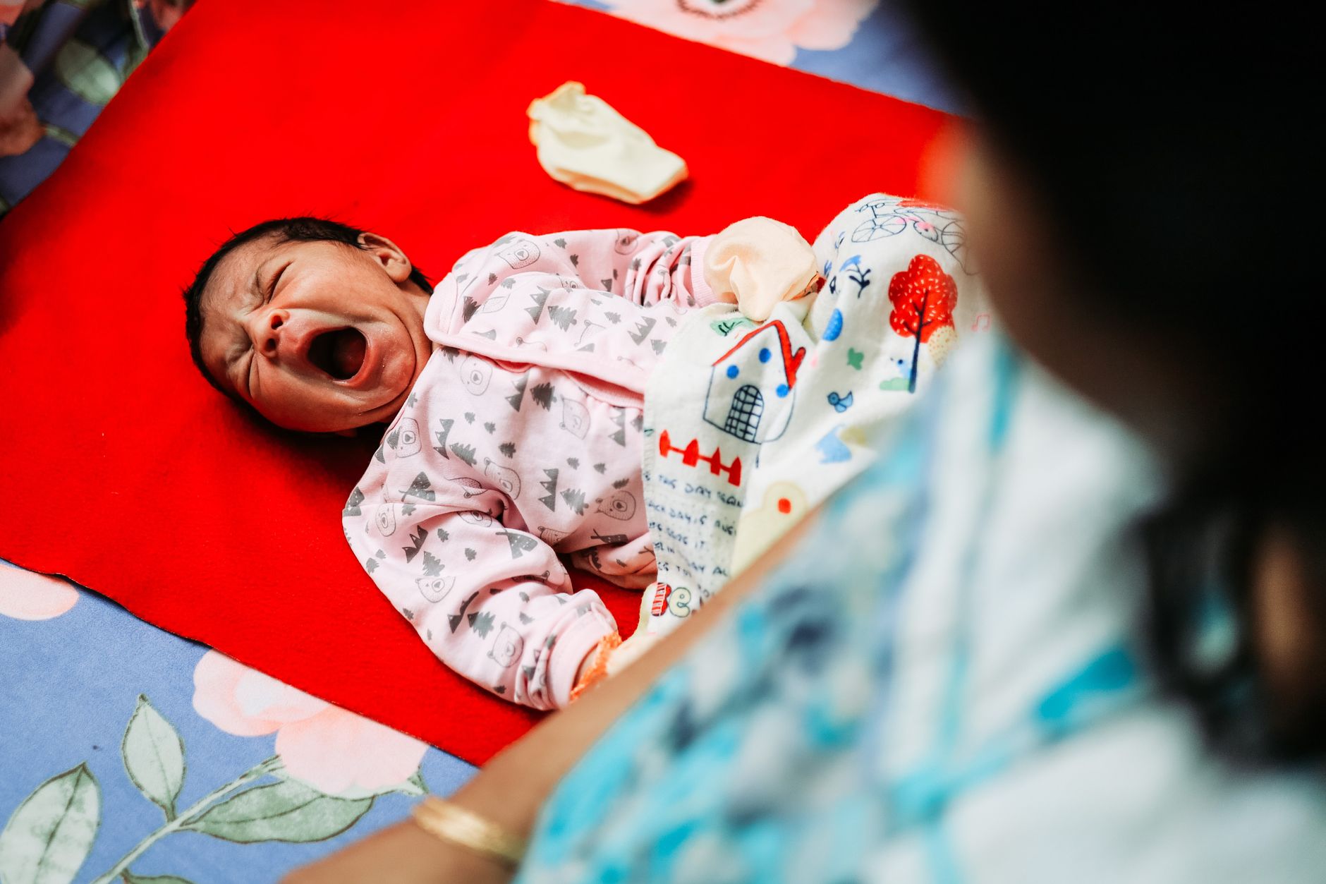 A calm mother holding a newborn on a soft blanket while reviewing a vaccination schedule on a tablet