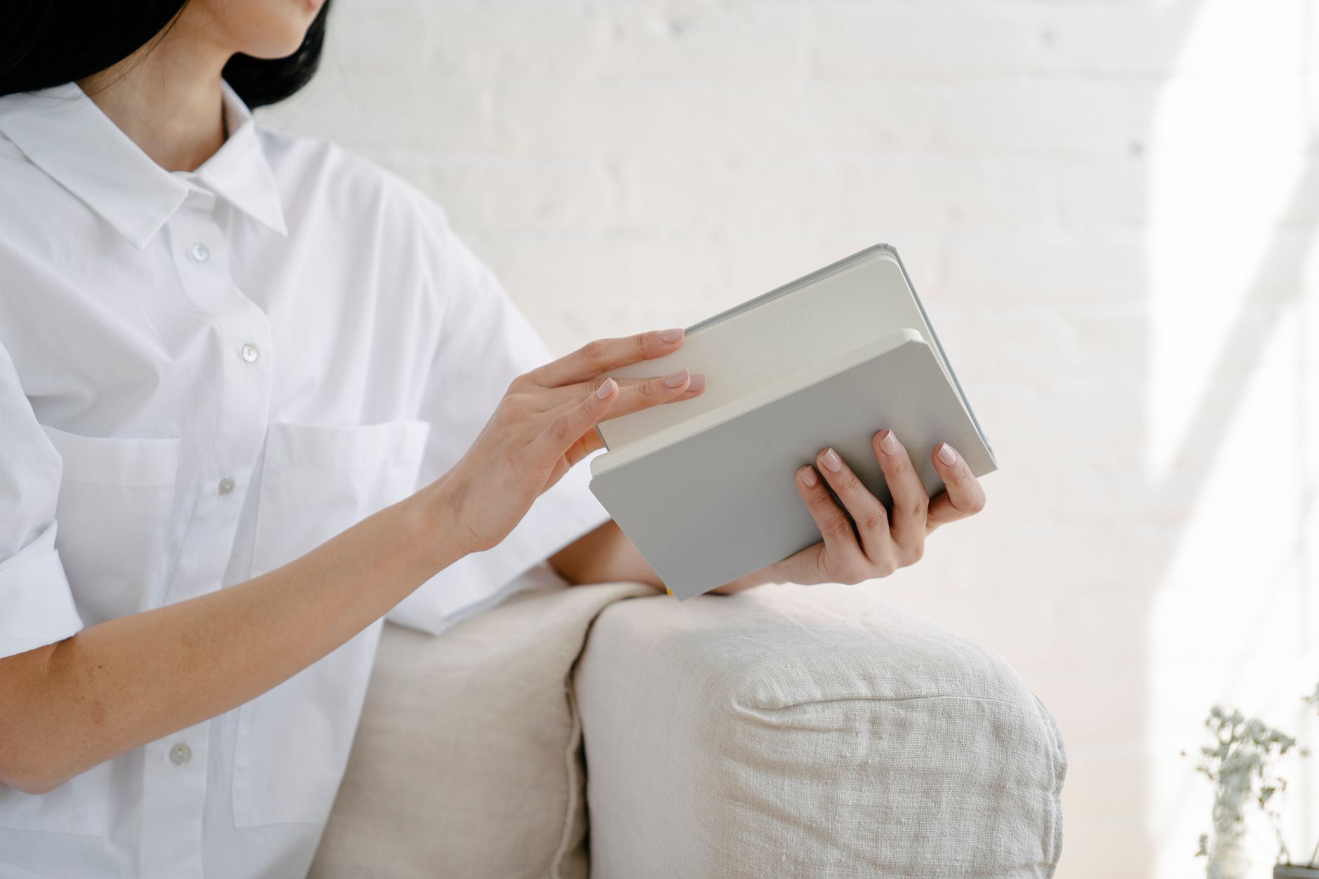 A mom sitting on the couch with a digital planner and a paper planner, deciding which one to use for postpartum recovery.