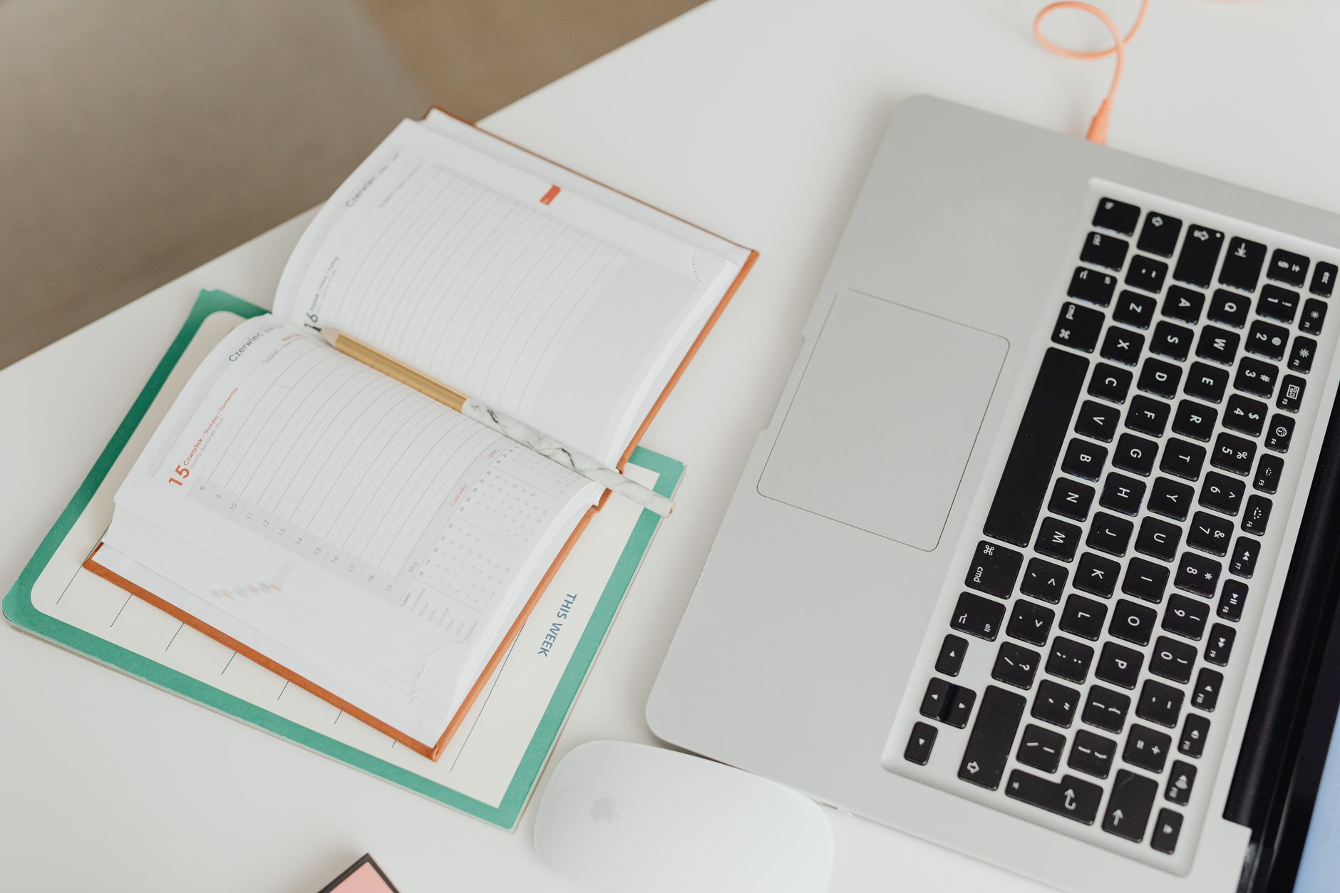 A mom sitting at a desk with a laptop and a notebook, deciding between a digital and paper planner.