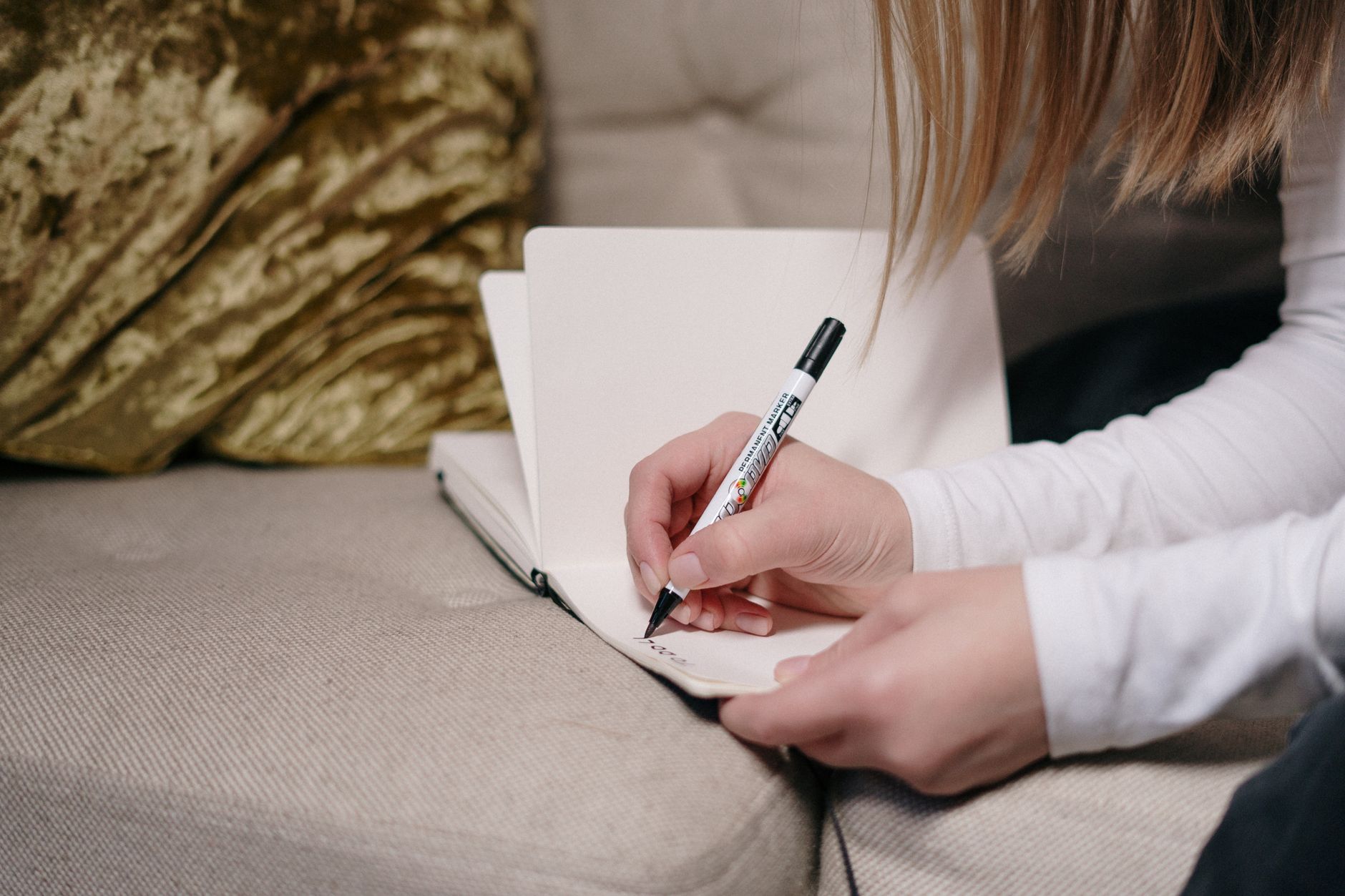 A new mom sitting on the couch with her newborn, writing in a paper planner.