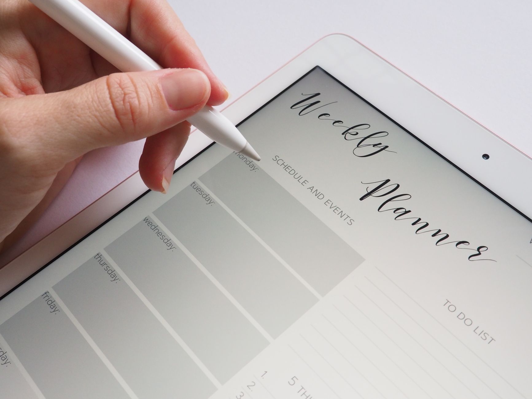 A pregnant woman smiling while organizing a digital planner on her tablet.