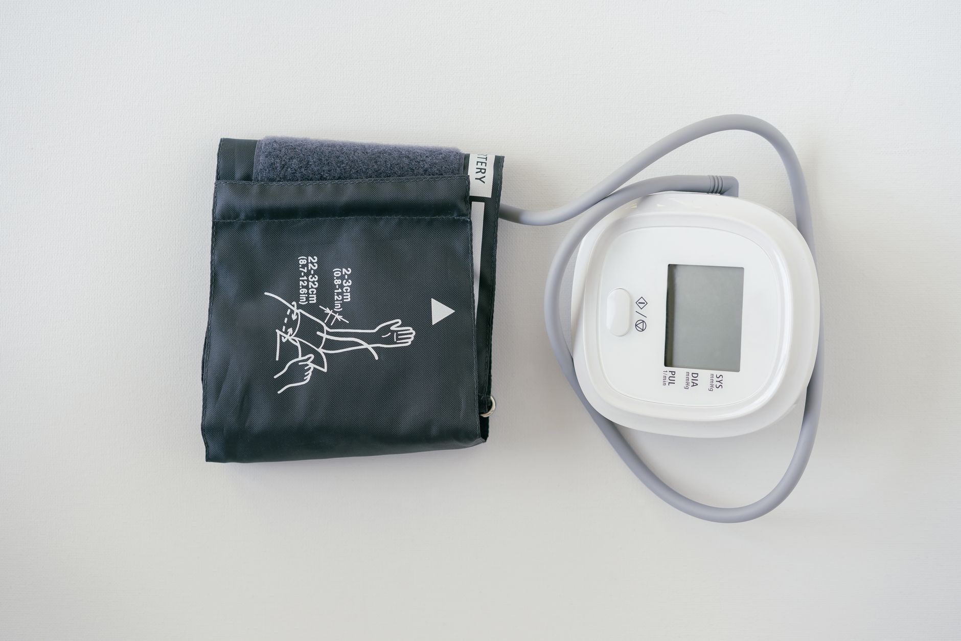 A digital blood pressure monitor cuff on a pregnant woman's arm, with a pen and notebook nearby on a clean surface, in a home setting
