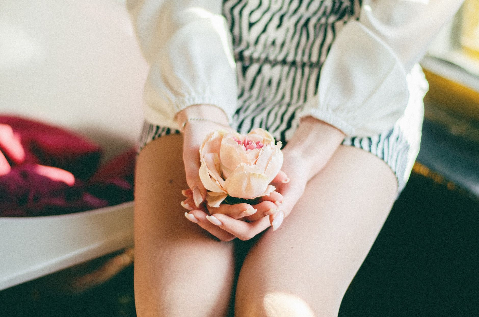 A person's hands gently rest on their lower abdomen, possibly indicating mild discomfort or a protective gesture, in a cozy, soft-lit setting