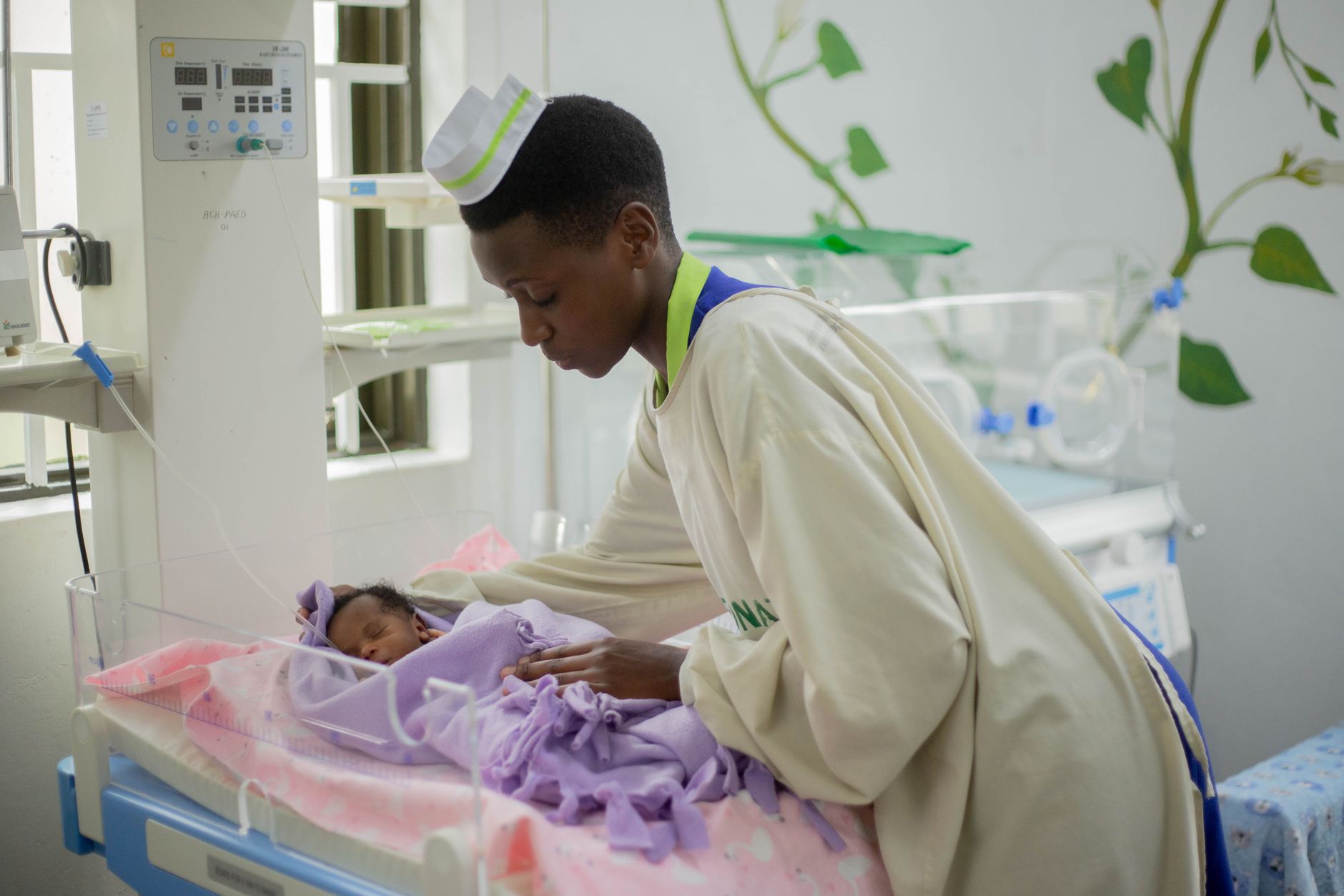 A NICU nurse gently adjusting a cooling blanket on a newborn baby in a crib