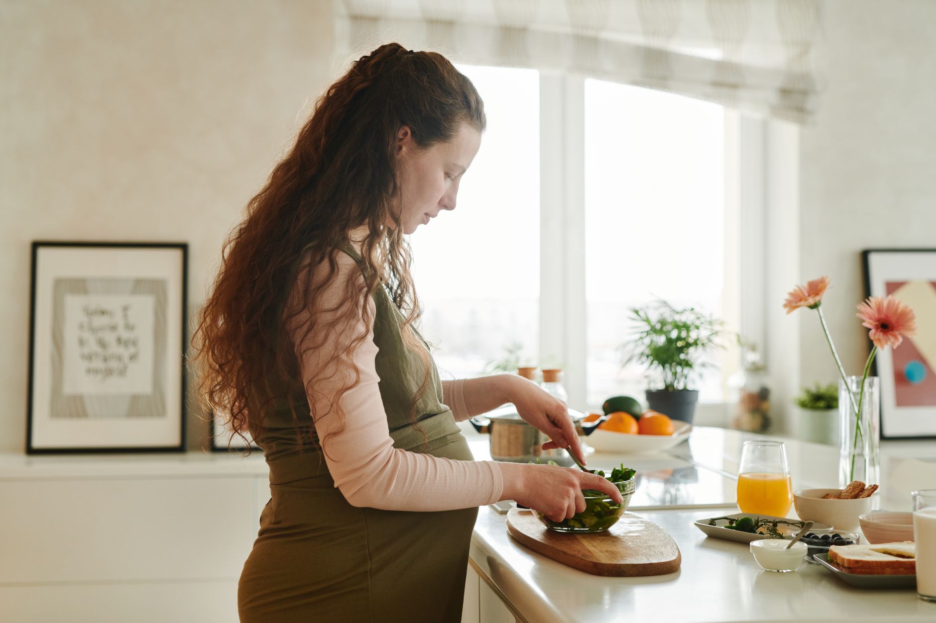 Pregnant woman holding a tablet showing a colorful Mayan gender chart, soft morning light on a kitchen counter