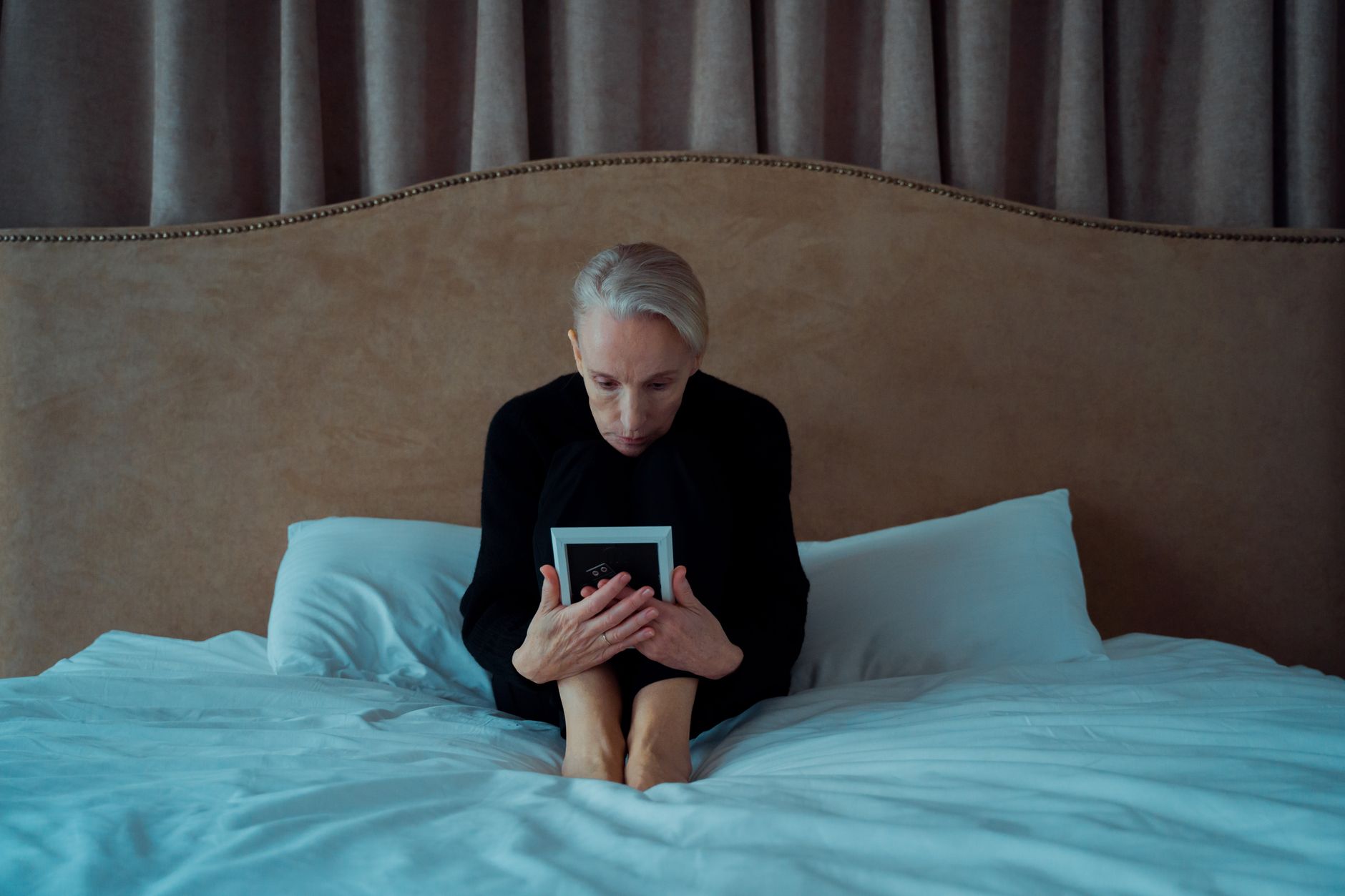 A woman sitting on a couch with a journal and tea, looking thoughtful, with a soft blanket draped over her shoulders
