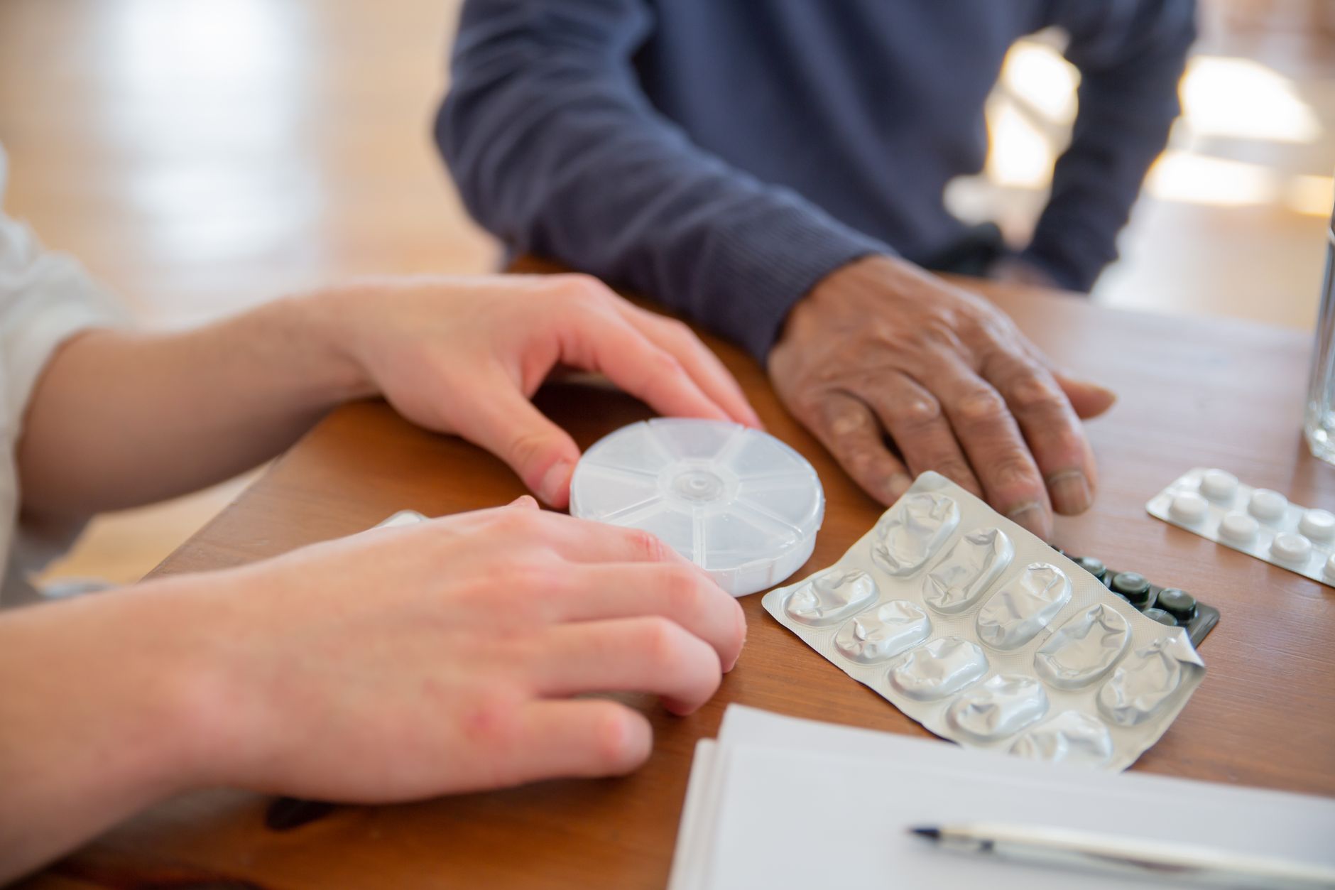 A bright, organized clinic room with a patient holding a medication schedule and a supportive partner