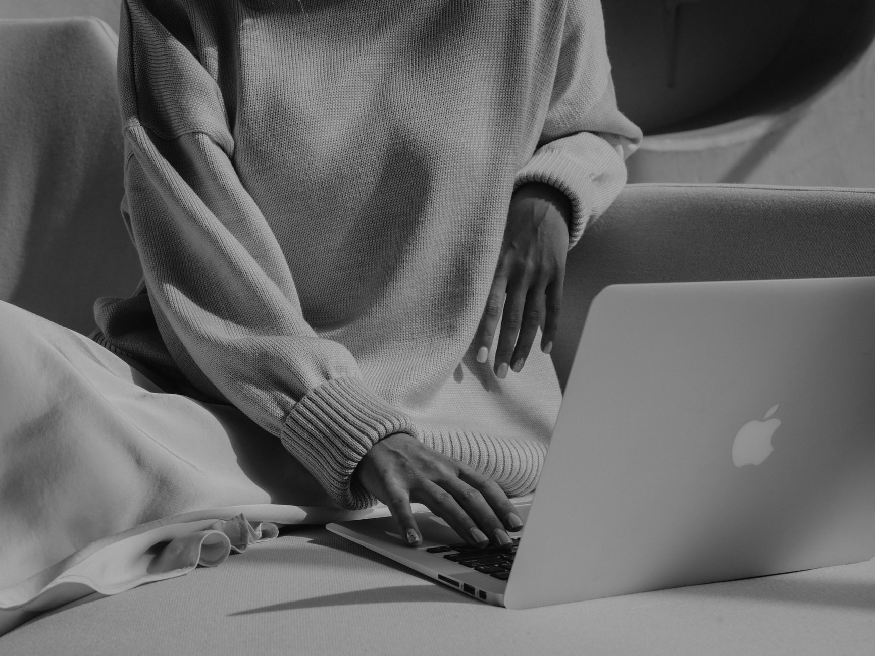 A woman in a cozy home office setting, using a hands-free breast pump while working on a laptop, soft natural light