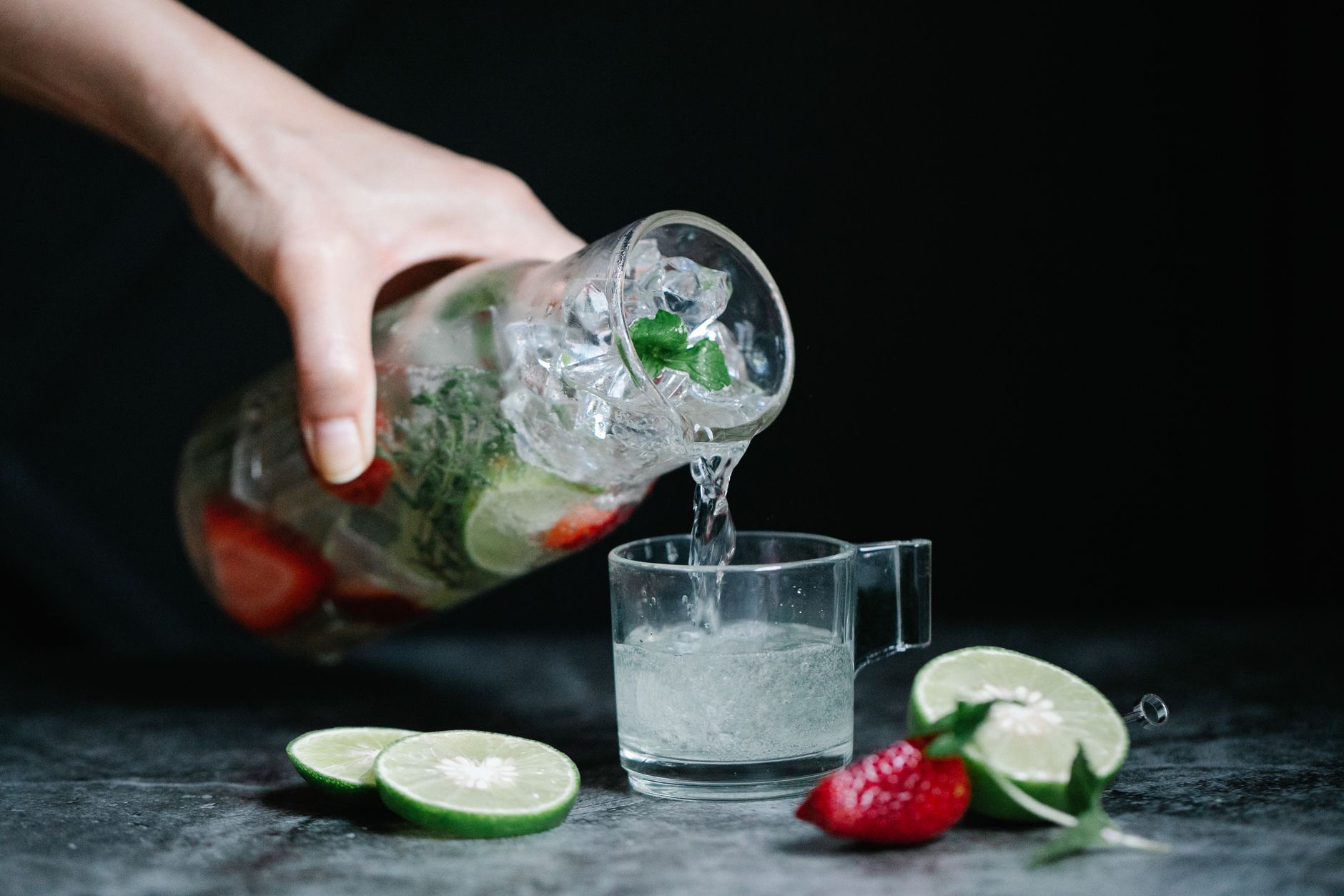 Close‑up of a glucose solution bottle, a hand pouring the liquid into a clear cup, bright kitchen light, fresh fruit in background