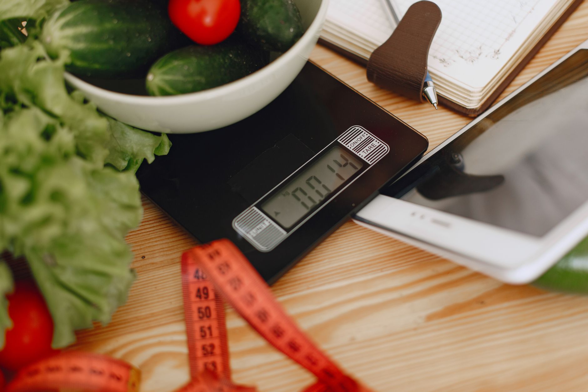 A bright kitchen counter with a digital baby scale, a measuring tape, and a notebook open to a growth chart, morning sunlight streaming in