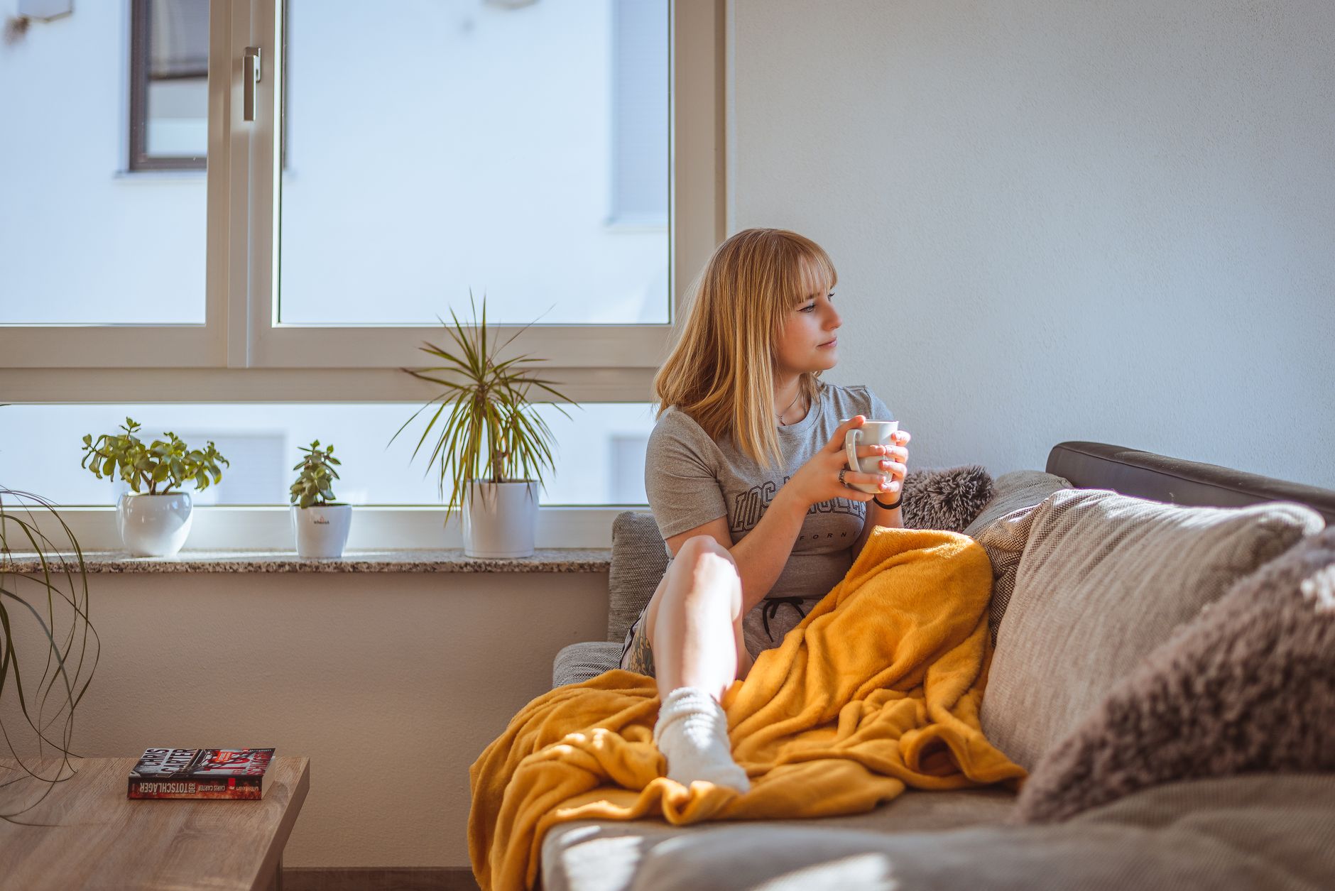 A pregnant woman resting on a couch with a cool compress on her forehead, soft natural light, cozy living room décor