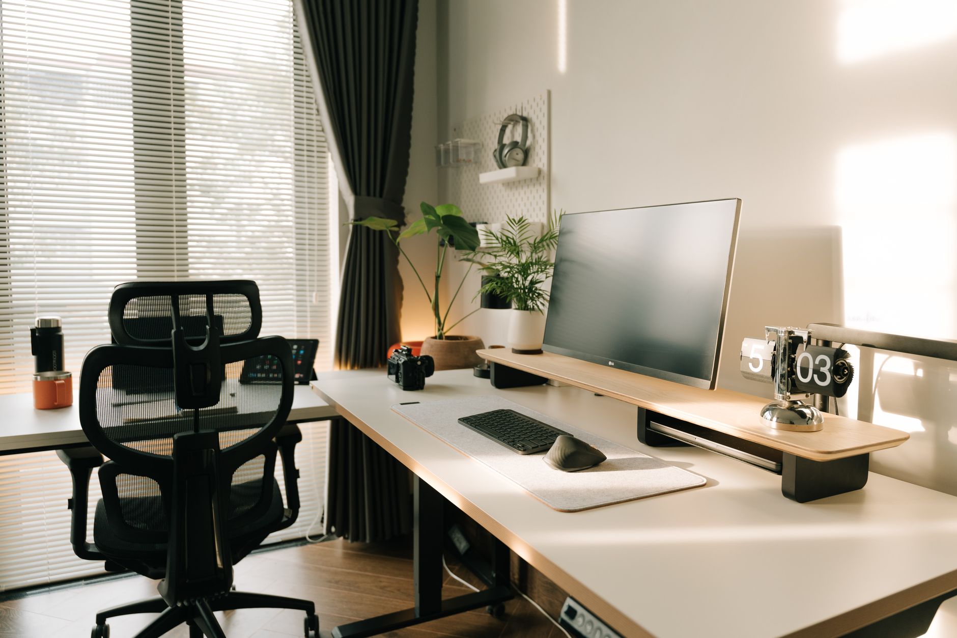 A tidy home office corner with a standing desk, ergonomic chair, and a whiteboard for to-do lists. A toddler plays quietly in a nearby playpen.