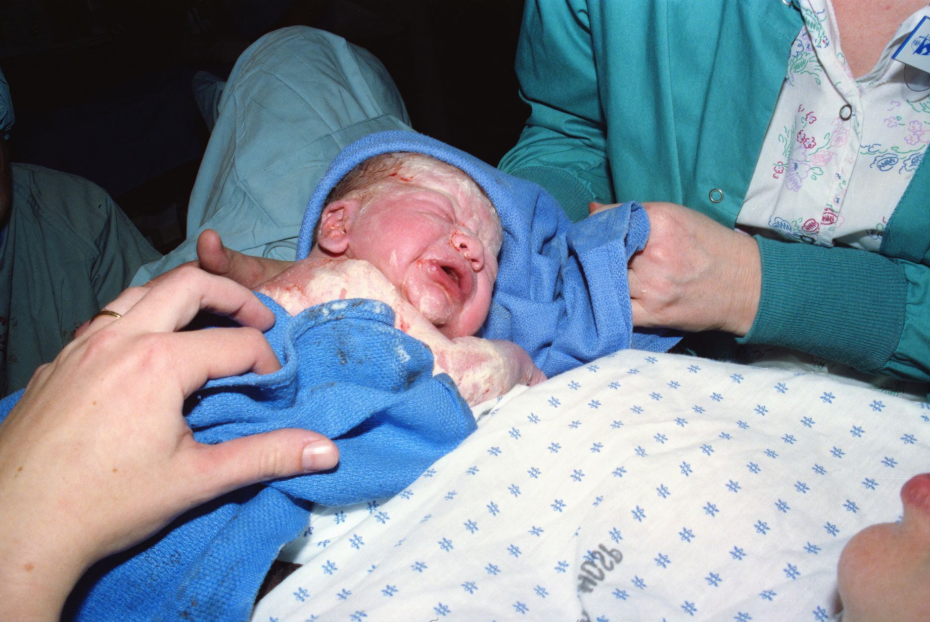 A close-up of a new mother's hands holding her baby's tiny feet, with a medical professional nearby
