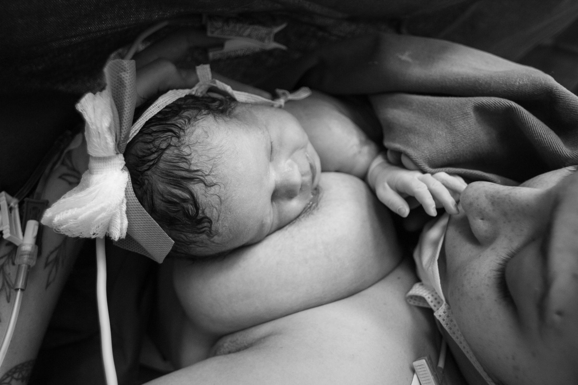 A new mother sitting on a hospital bed, holding her baby and looking exhausted but content