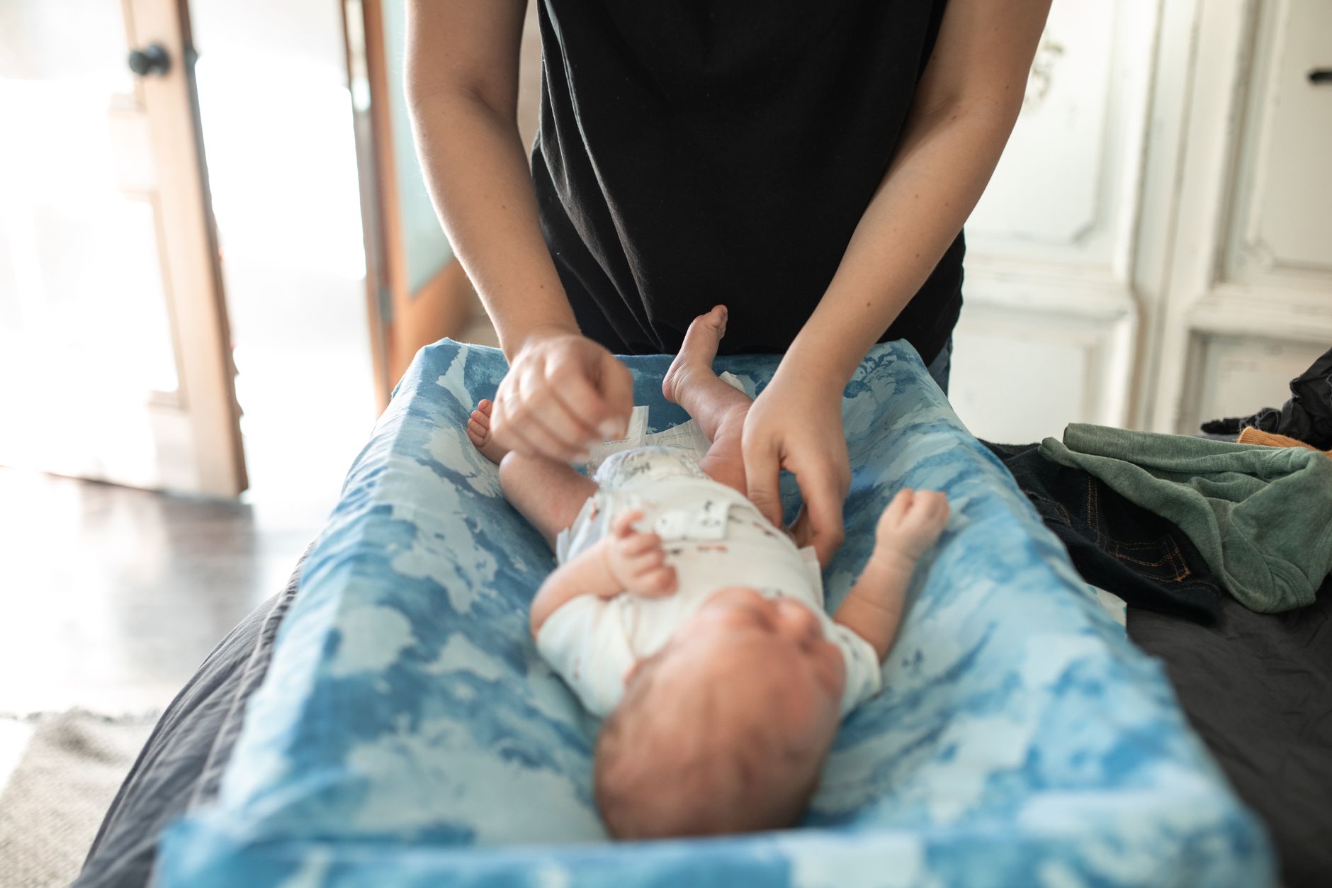 A mom changing a newborn's diaper with a cream and wipes nearby