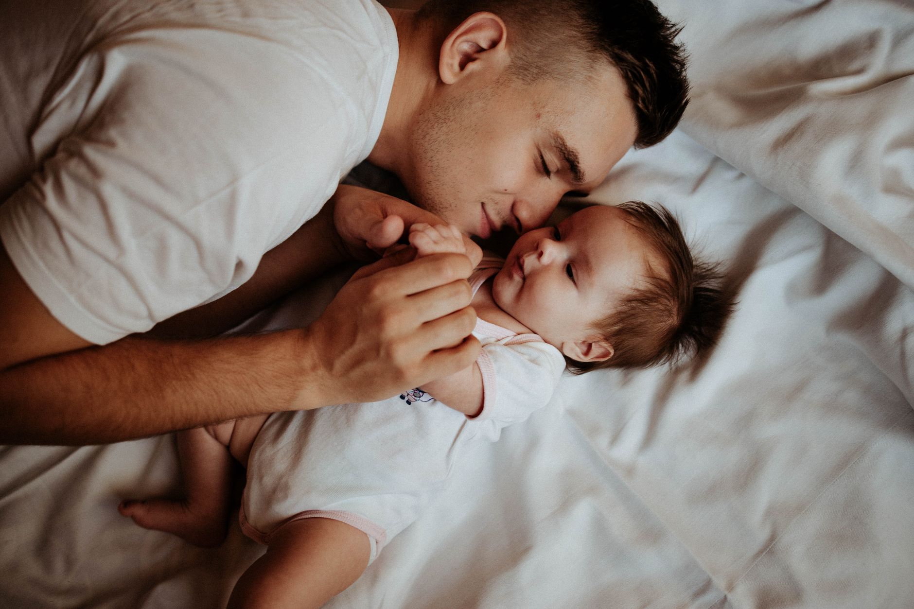 A mom and dad holding their newborn baby together, smiling and looking at each other