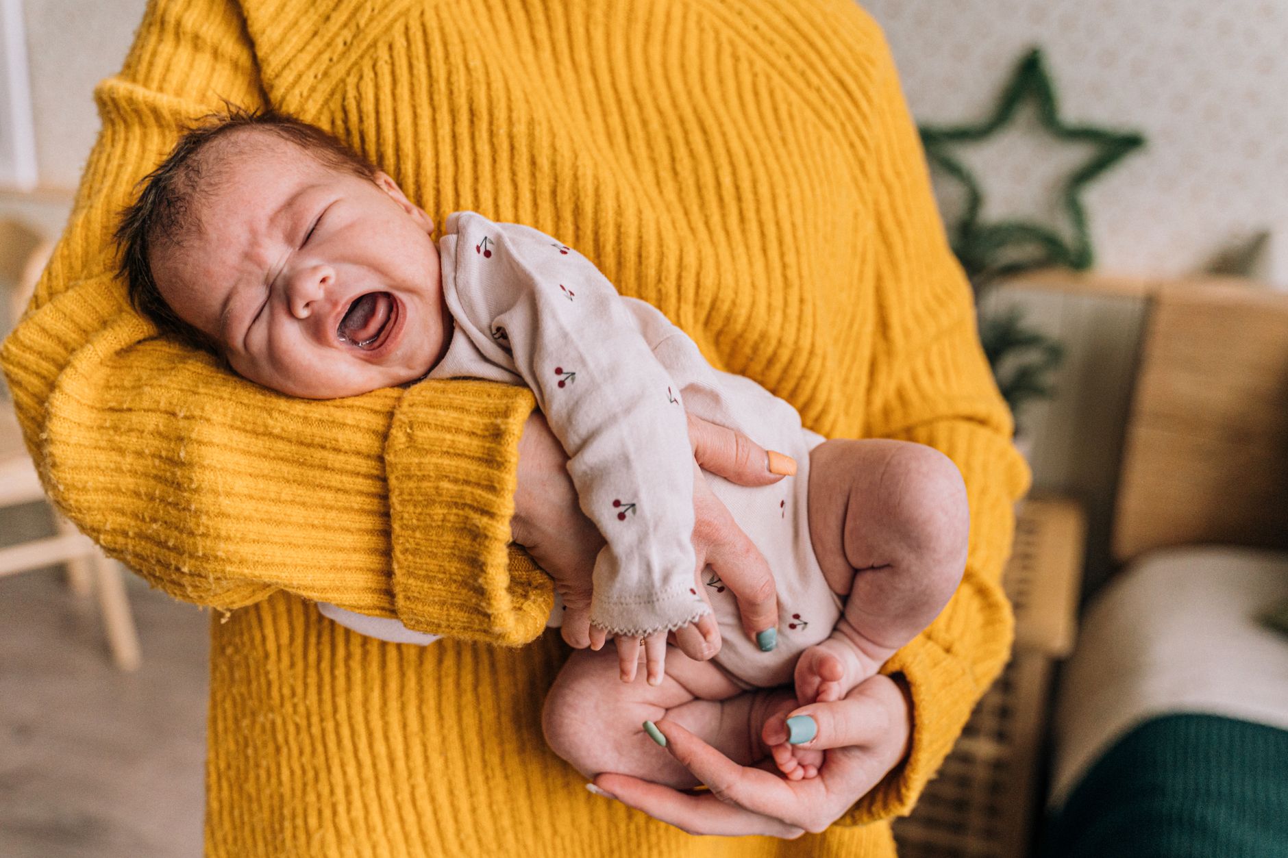 A mom rocking her fussy newborn in a sling while looking out a window