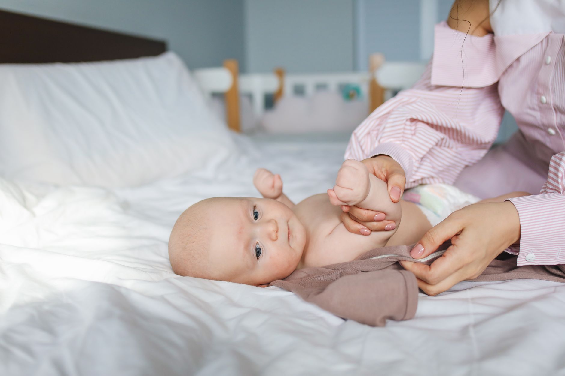 A first-time mom sitting on a bed, holding her baby’s tiny hand, looking thoughtful
