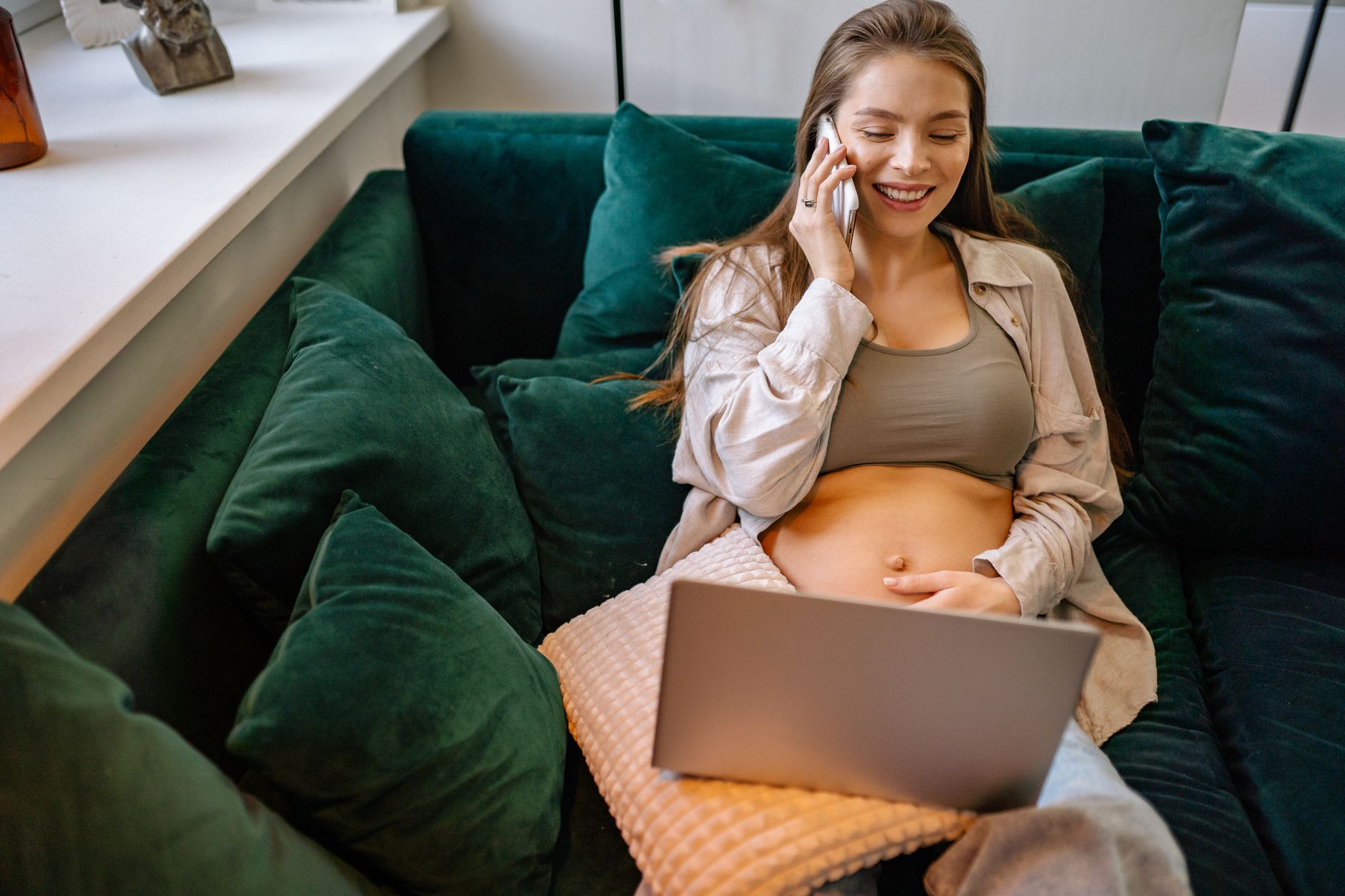 Pregnant woman sitting on a couch, holding her belly and looking at her phone with a concerned expression