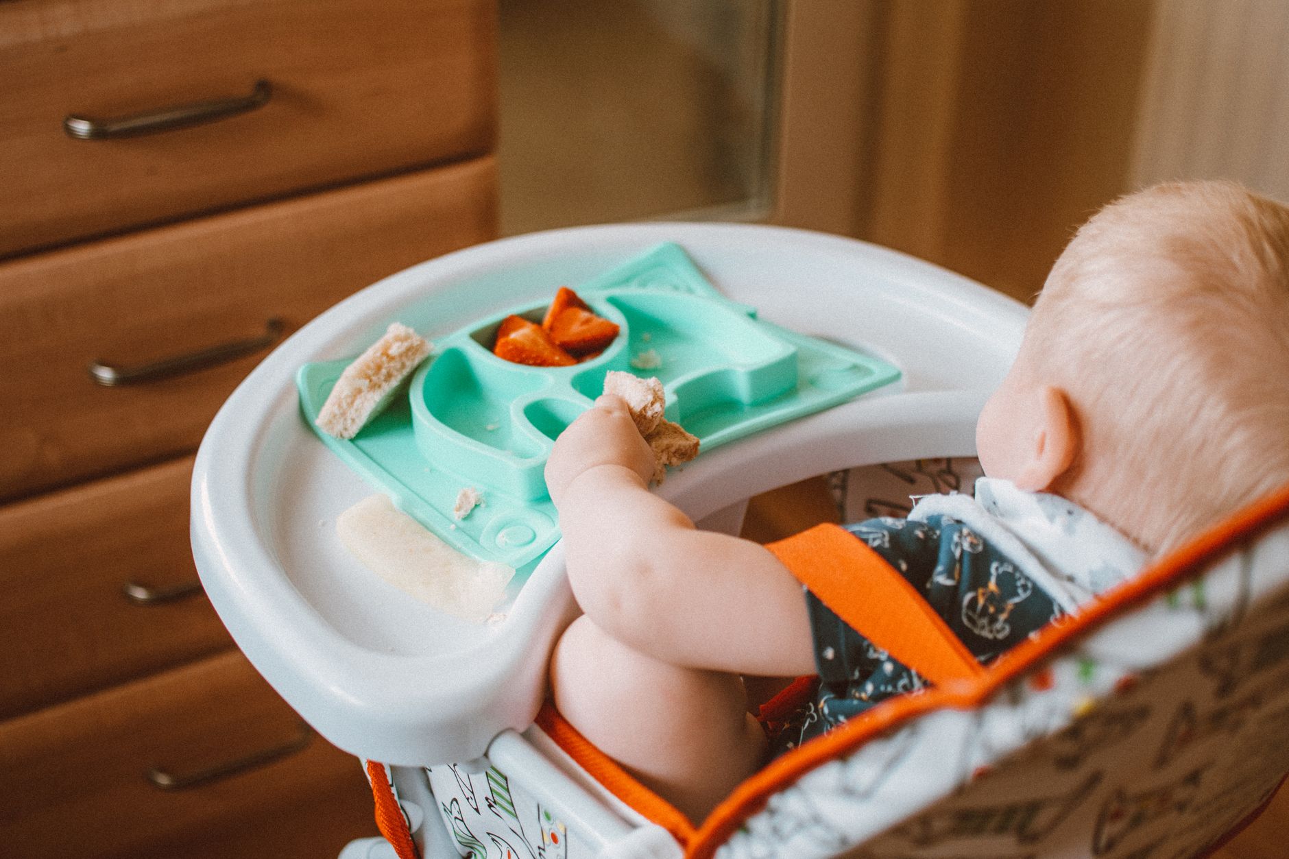 A toddler sitting in a high chair with a deep tray and footrest, with a silicone placemat underneath