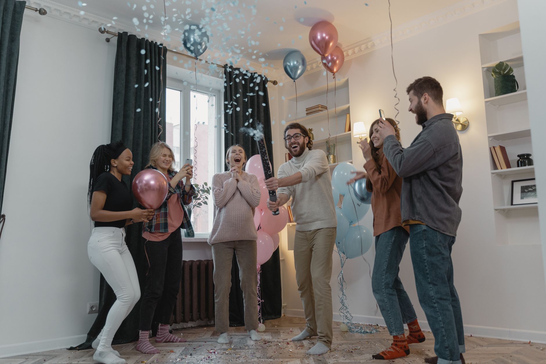 A joyful couple smiling as blue confetti bursts around them, revealing the baby's gender, with excited friends in the background