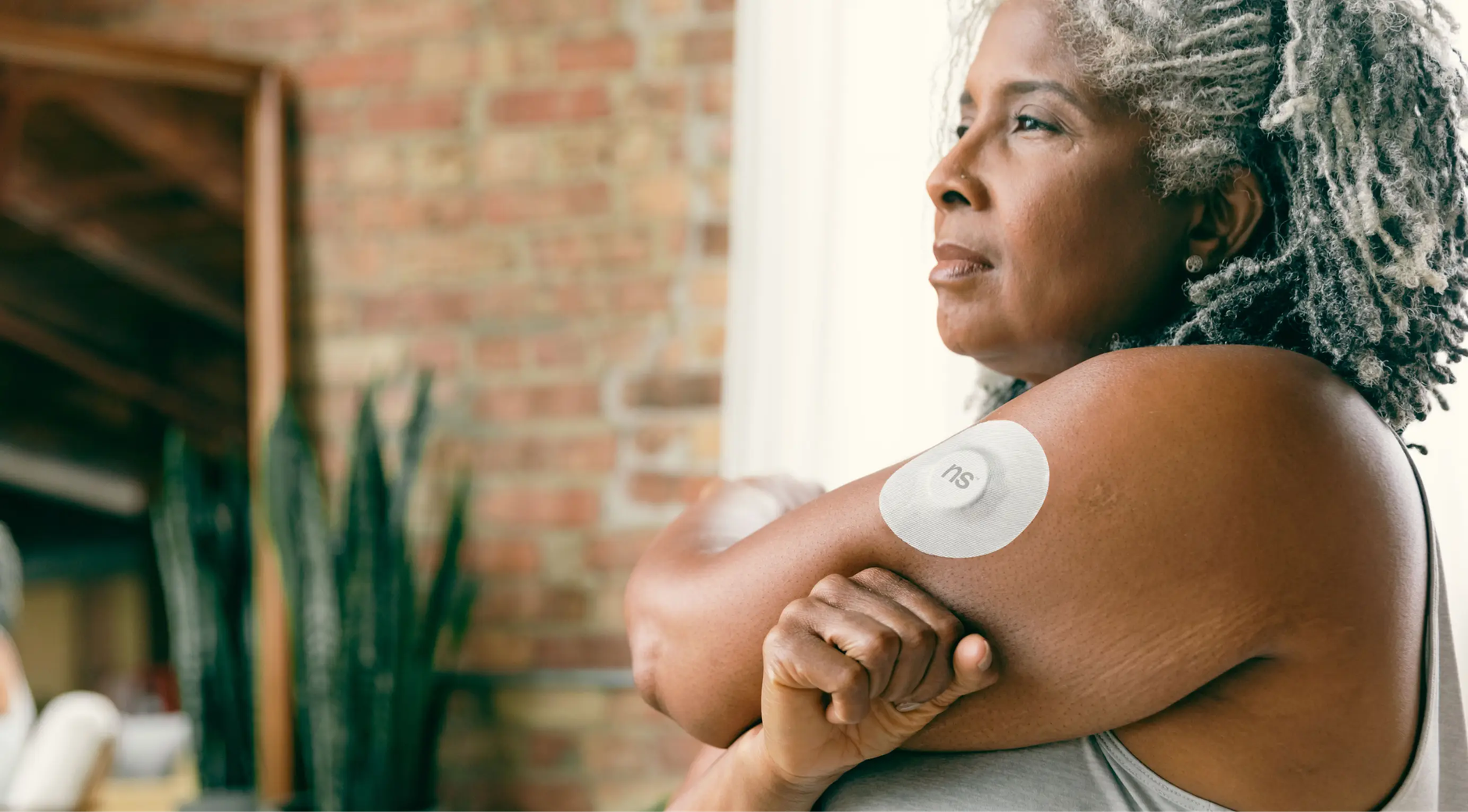Close‑up of a continuous glucose monitor sensor on a woman's forearm, soft indoor lighting, with a smartphone displaying glucose trend graph