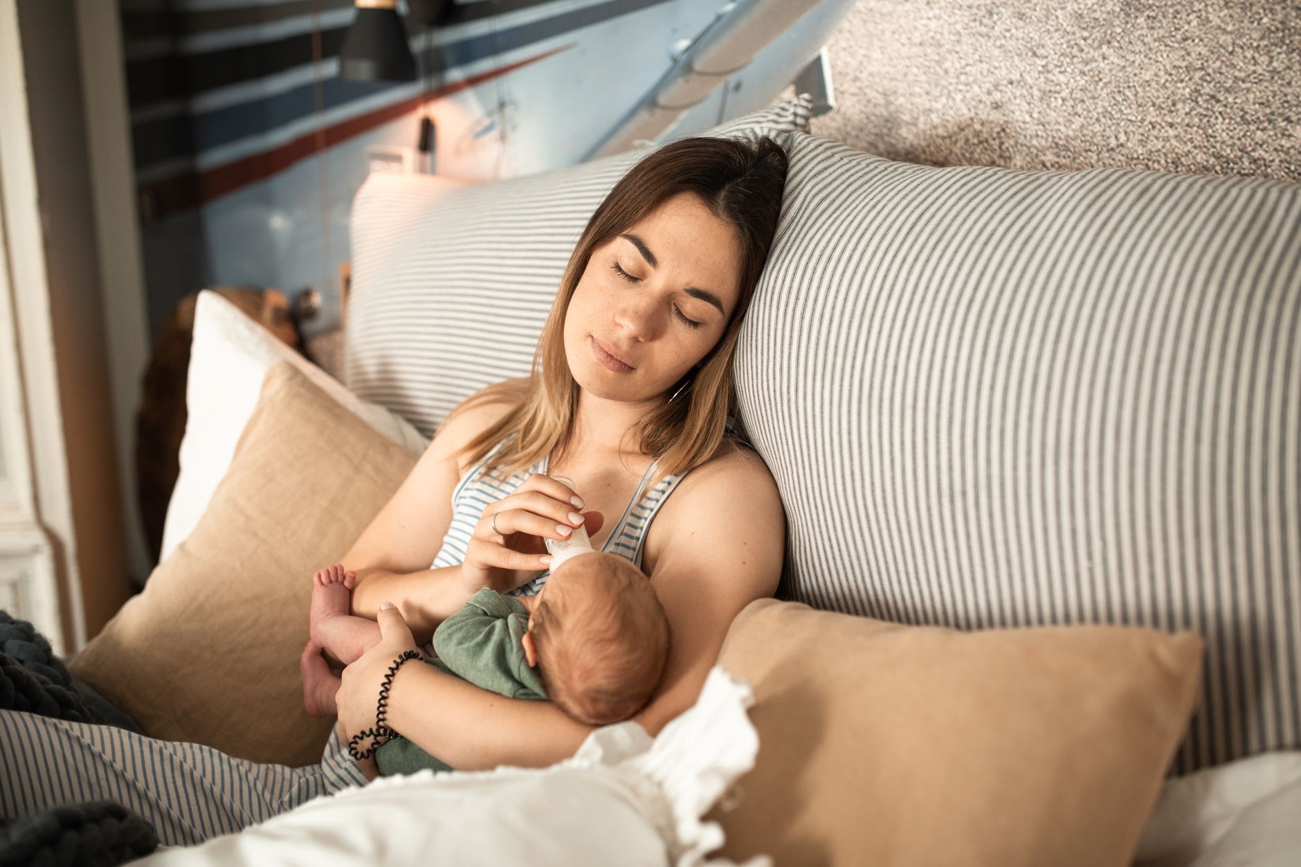 New mother holding a newborn baby in a softly lit bedroom, gentle morning light through the window, calm and supportive atmosphere