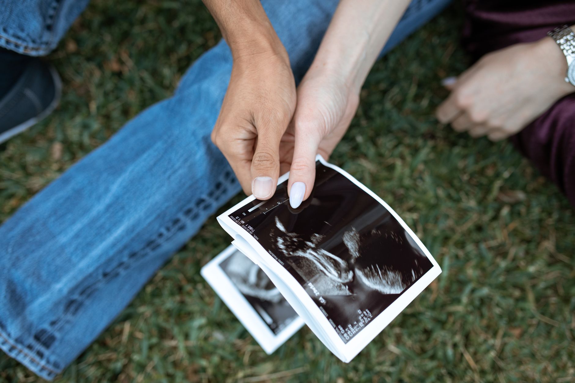 A hand holding a pregnancy ultrasound photo next to a framed photo of a grandmother