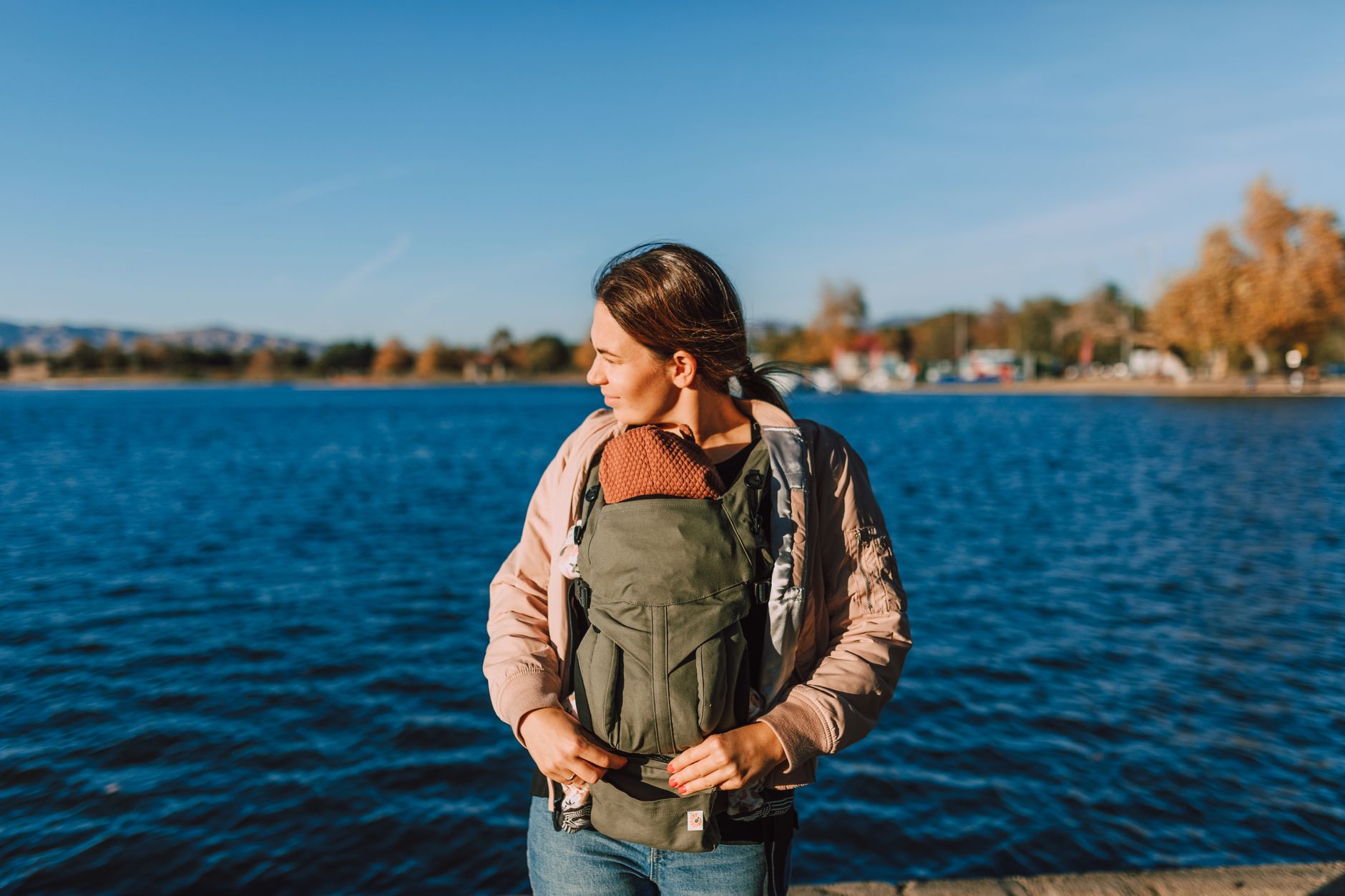 A mom wearing her baby in an ergonomic carrier, smiling while walking through a park with her partner