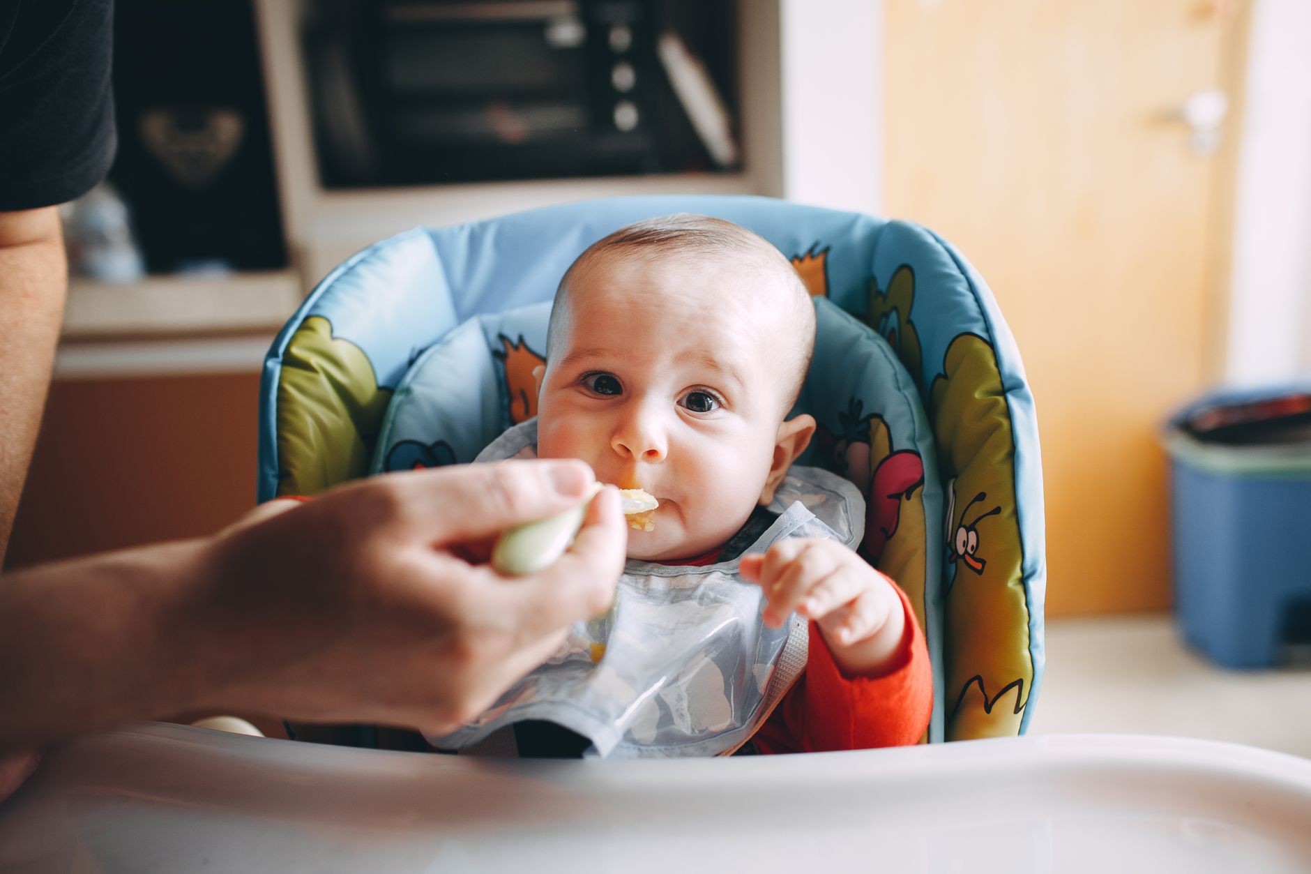 A baby happily eating pureed food in a high chair, with a parent and grandparent smiling.