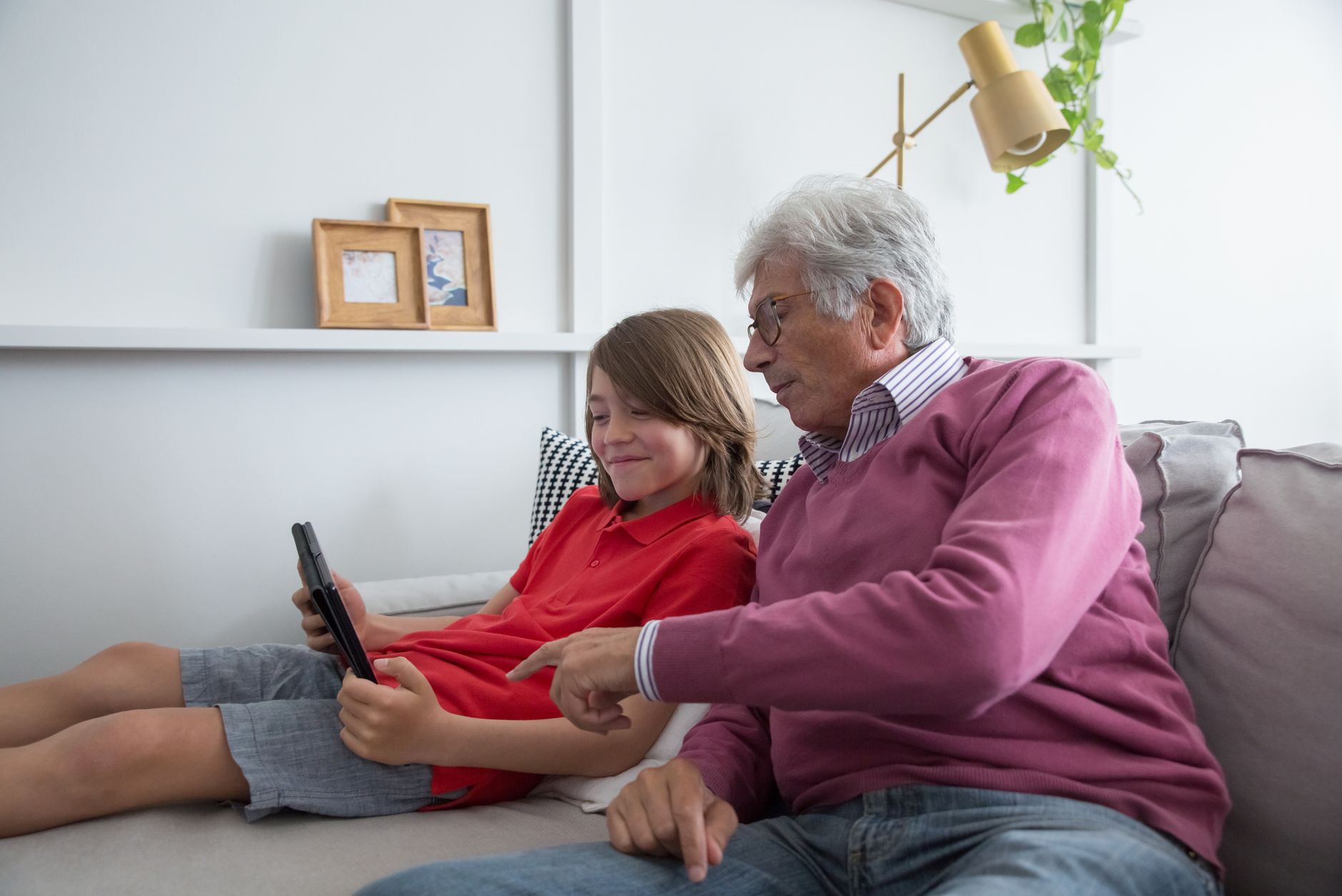 A toddler sitting on a grandparent’s lap, watching a tablet together with a smile